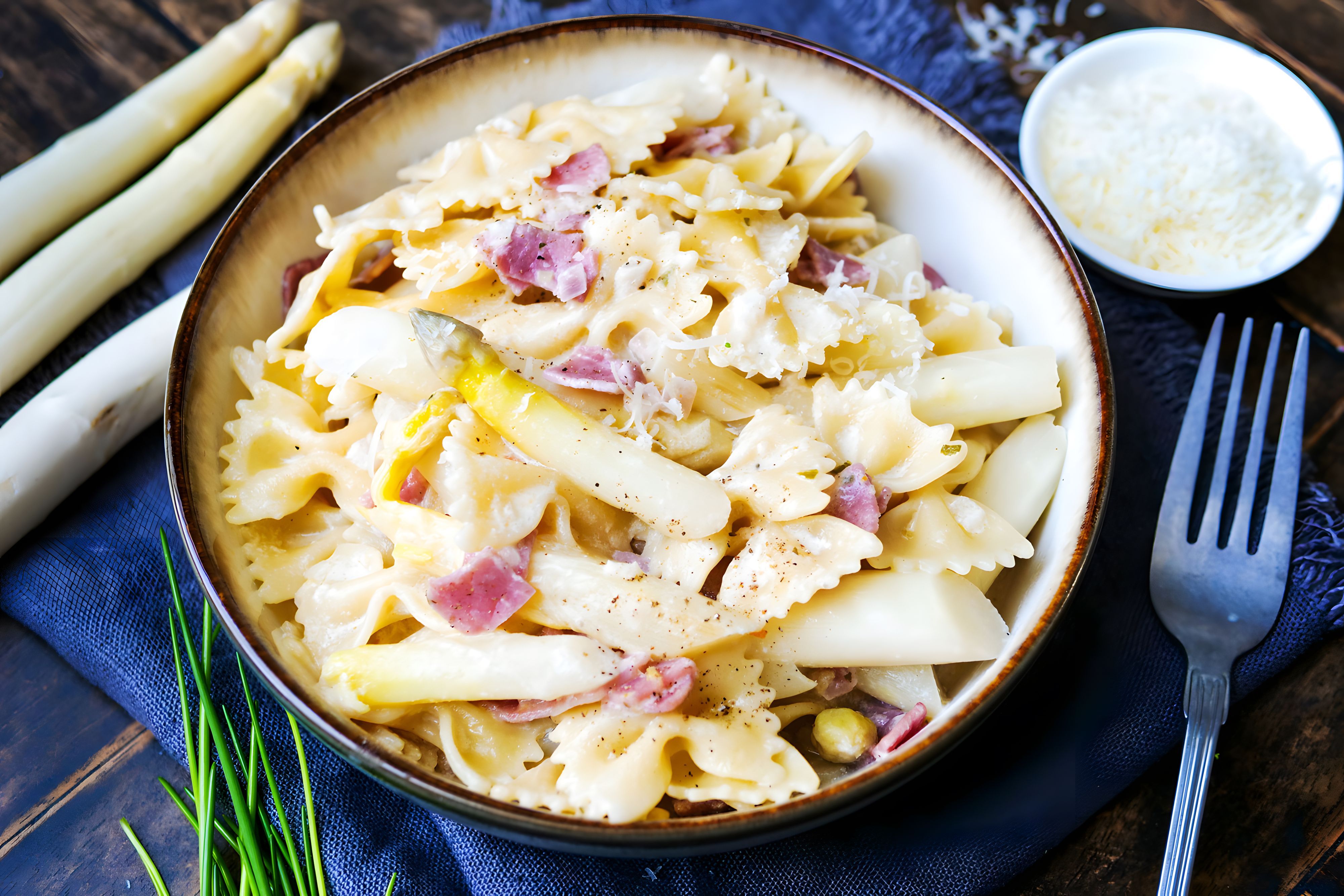 Auf einem Teller ist ein Gericht aus Nudeln mit Spargel und Schinken angerichtet.