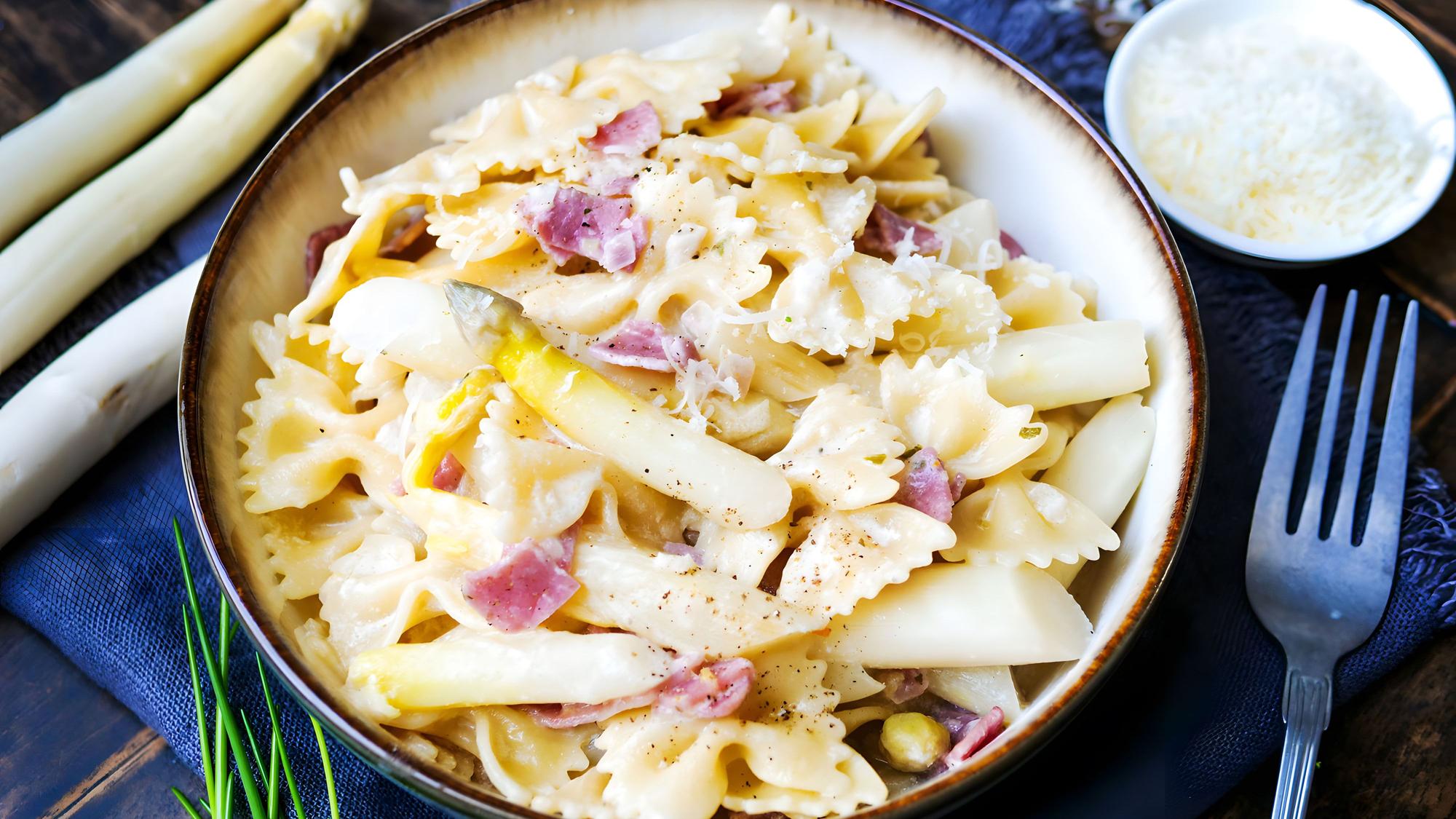 Auf einem Teller ist ein Gericht aus Nudeln mit Spargel und Schinken angerichtet.