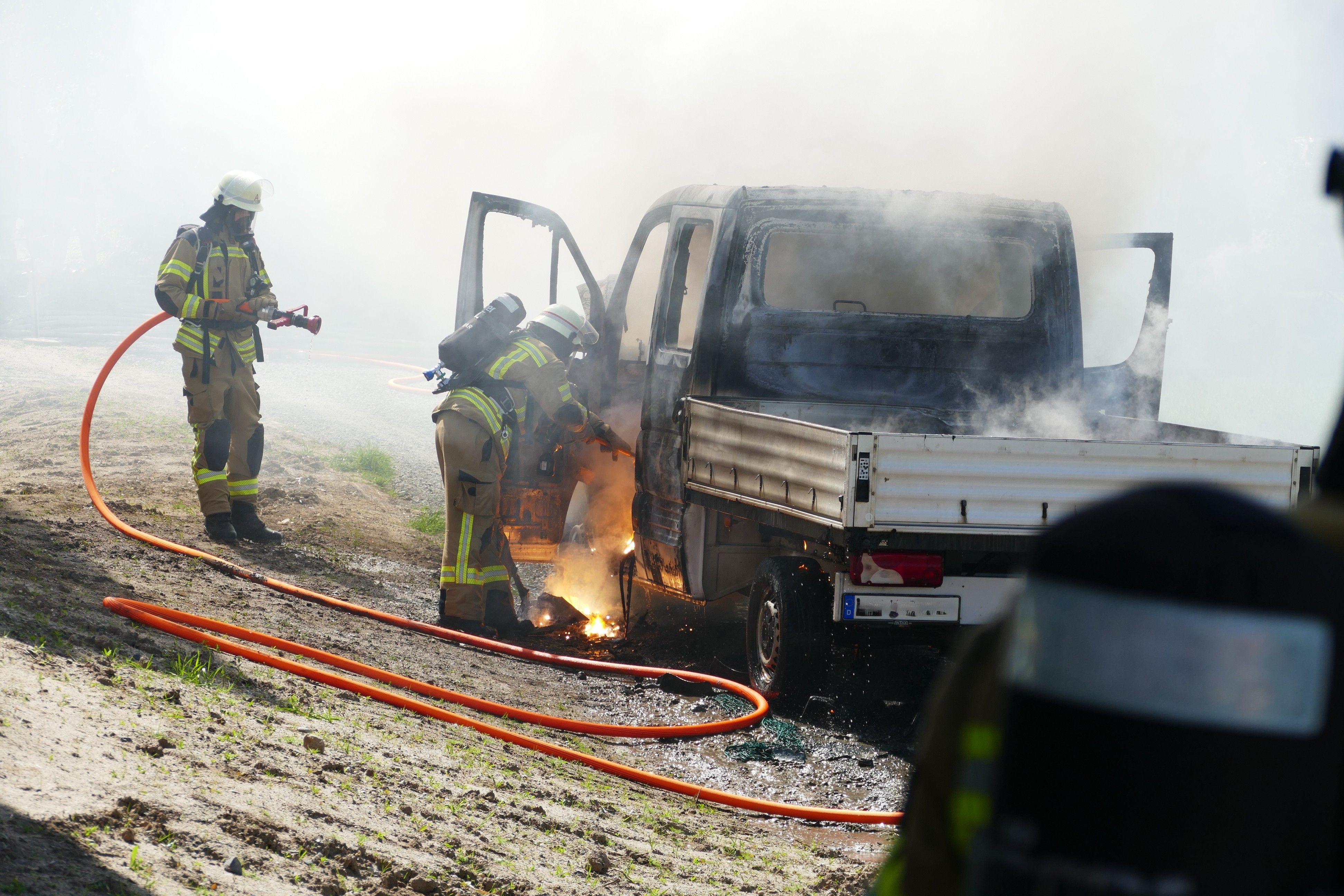 Feuerwehrleute im Einsatz an einem brennenden Pritschenwagen.