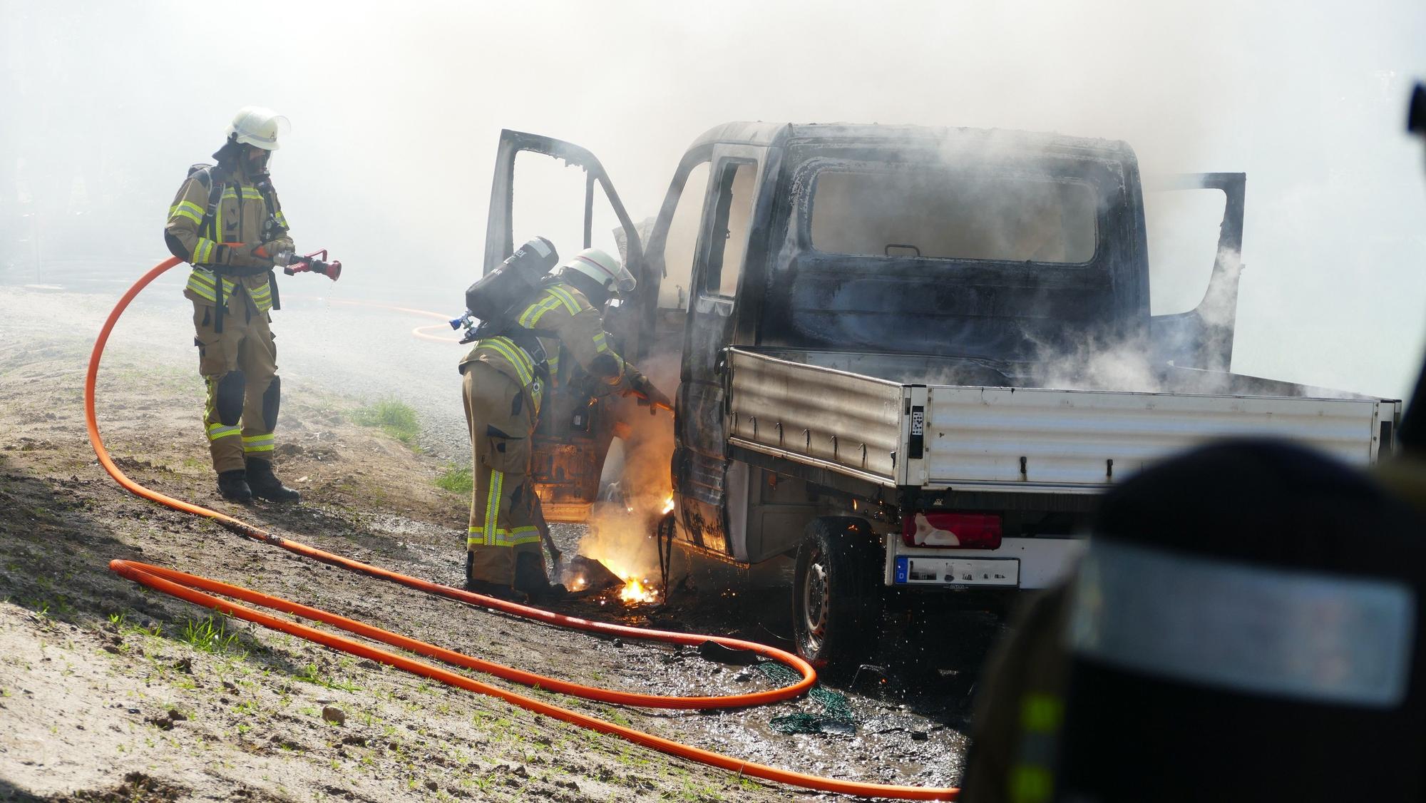 Feuerwehrleute im Einsatz an einem brennenden Pritschenwagen.