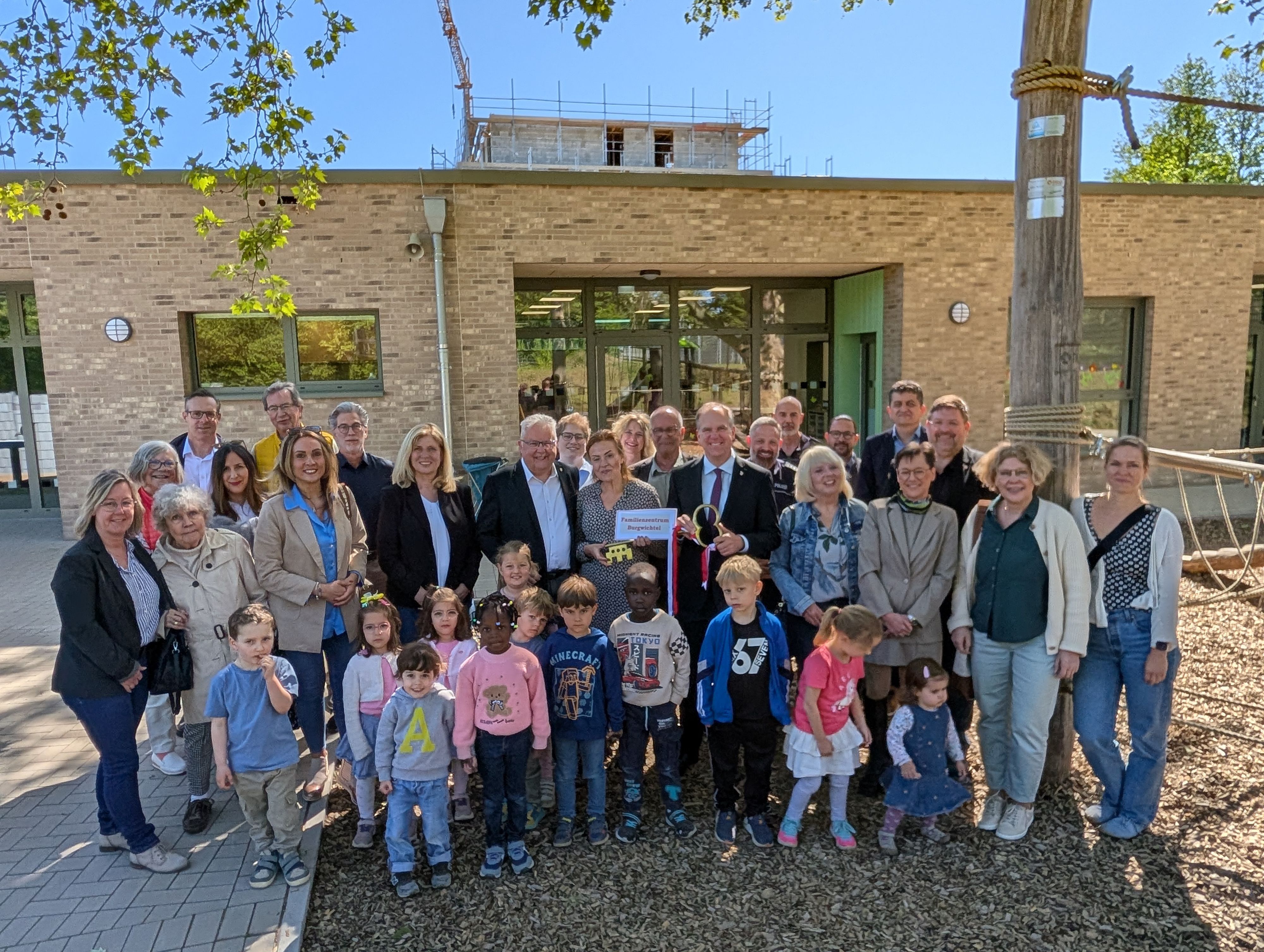 Das Foto zeigt eine große Gruppe von Gästen und Kindern bei der Schlüsselübergabe vor der Kita.