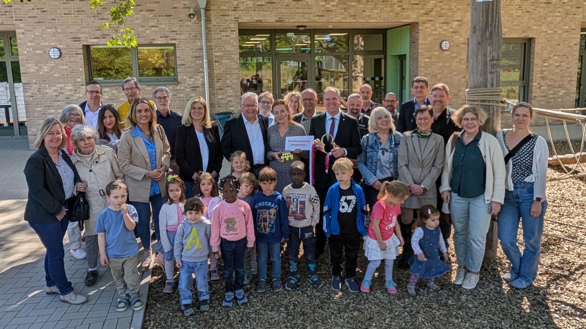 Das Foto zeigt eine große Gruppe von Gästen und Kindern bei der Schlüsselübergabe vor der Kita.