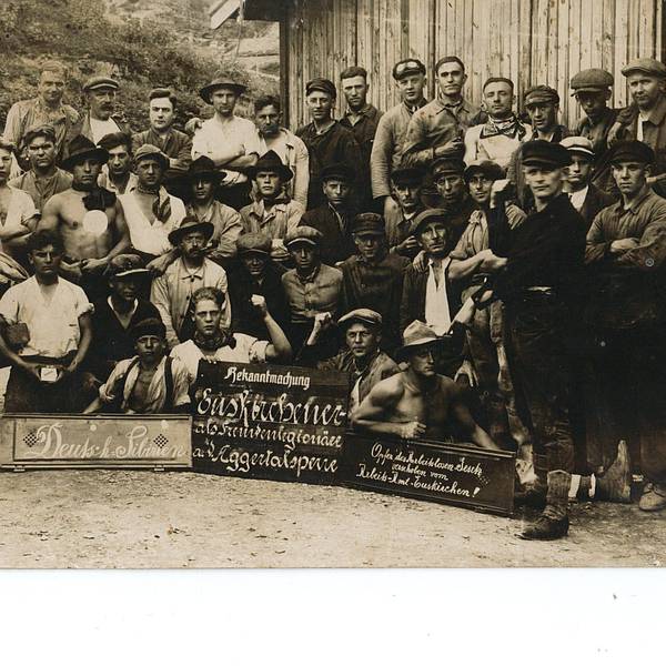 Dies ist die Vorderseite einer nicht gelaufenen Postkarte. Die Fotografie zeigt offensichtlich unzufriedene Arbeiter aus dem Raum Euskirchen, die sich laut einem Schild als „Opfer des Arbeitslosengesetzes“ sehen, beim Bau der Aggertalsperre bei Gummersbach, vermutlich 1927.