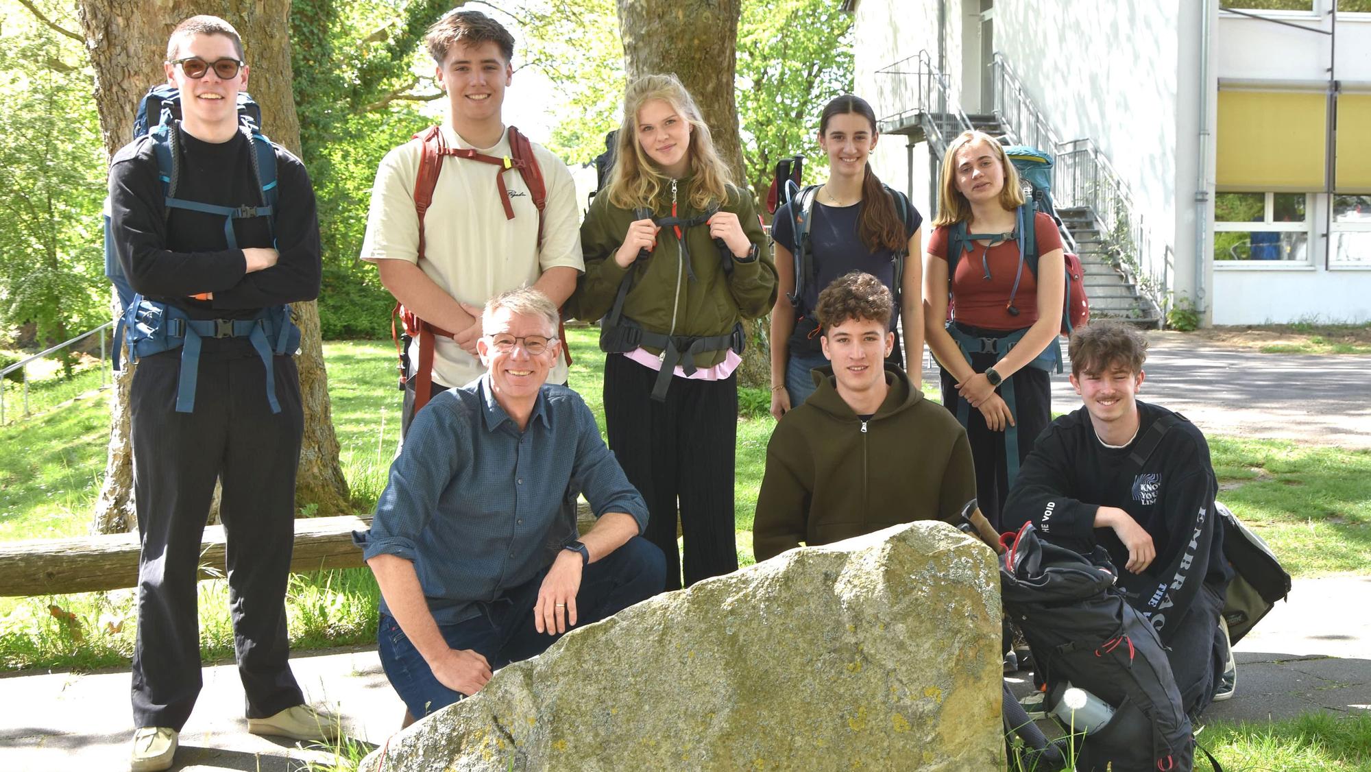 Schüler stehen und knien um einen großen Stein herum auf einem Schulgelände.