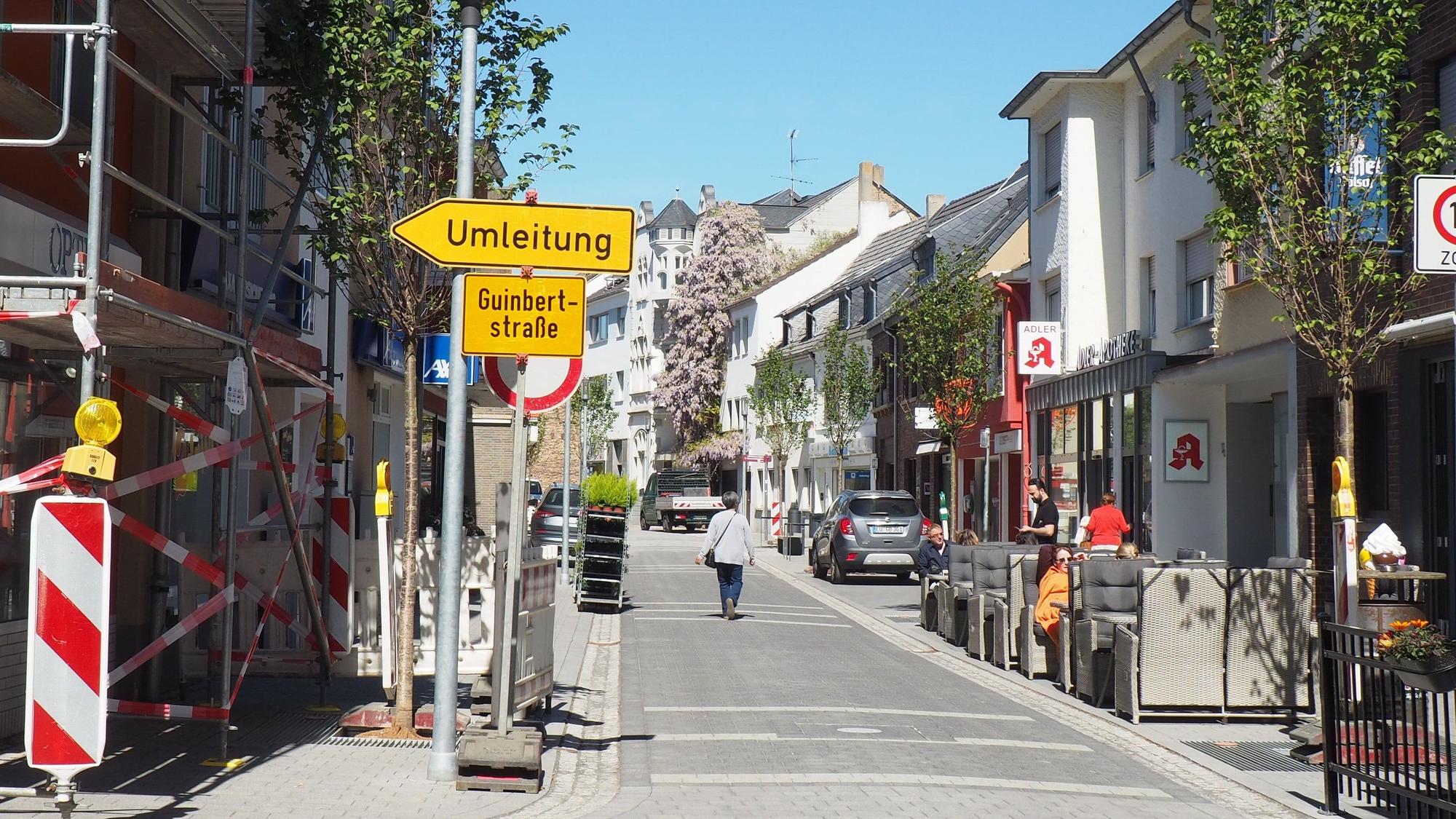 Ein Blick auf die Münsterstraße. Links stehen Baugerüste und ein Umleitungsschild, rechts sitzen Menschen in einem Straßencafé.