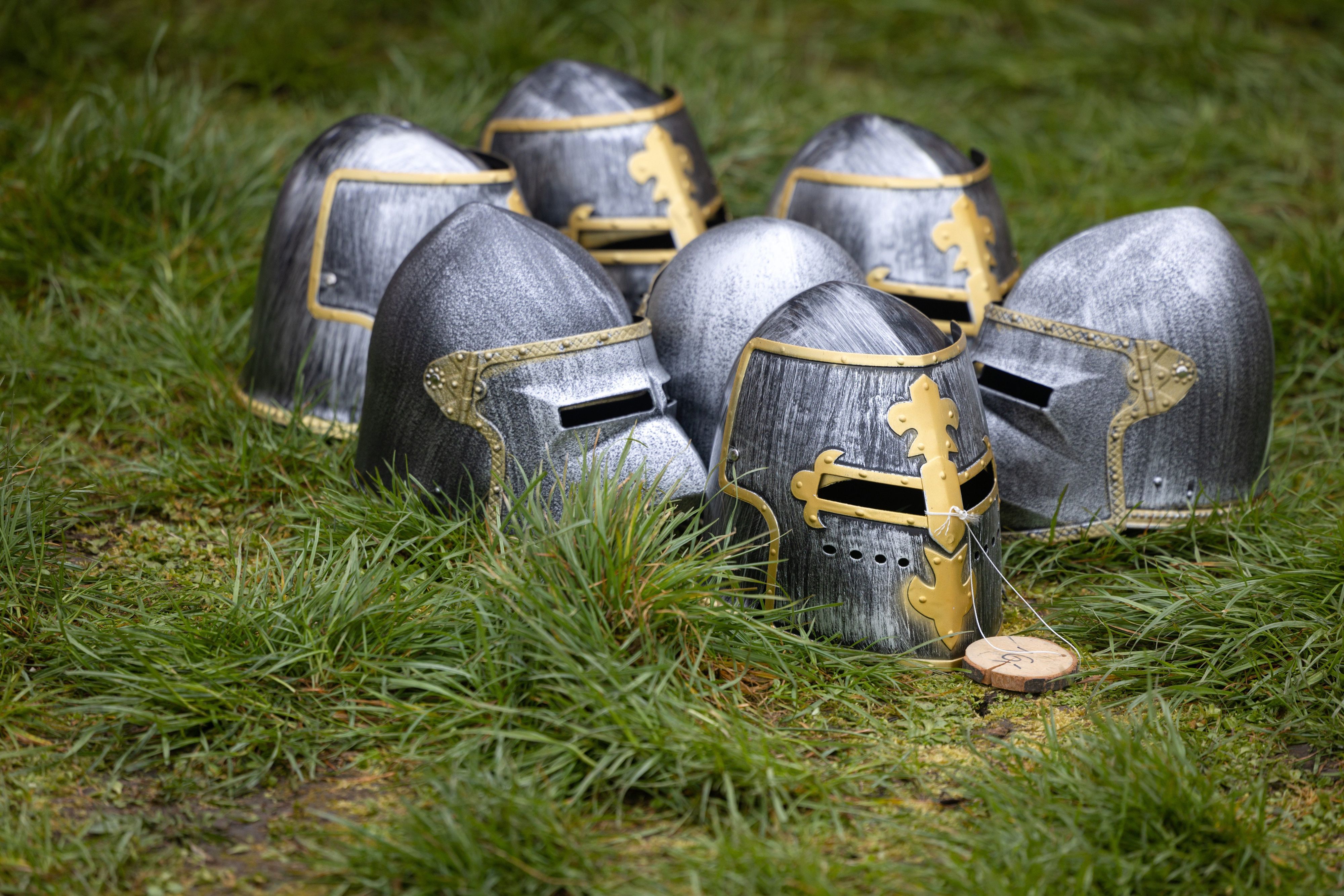Mehrere Ritterhelme liegen auf einer Wiese.