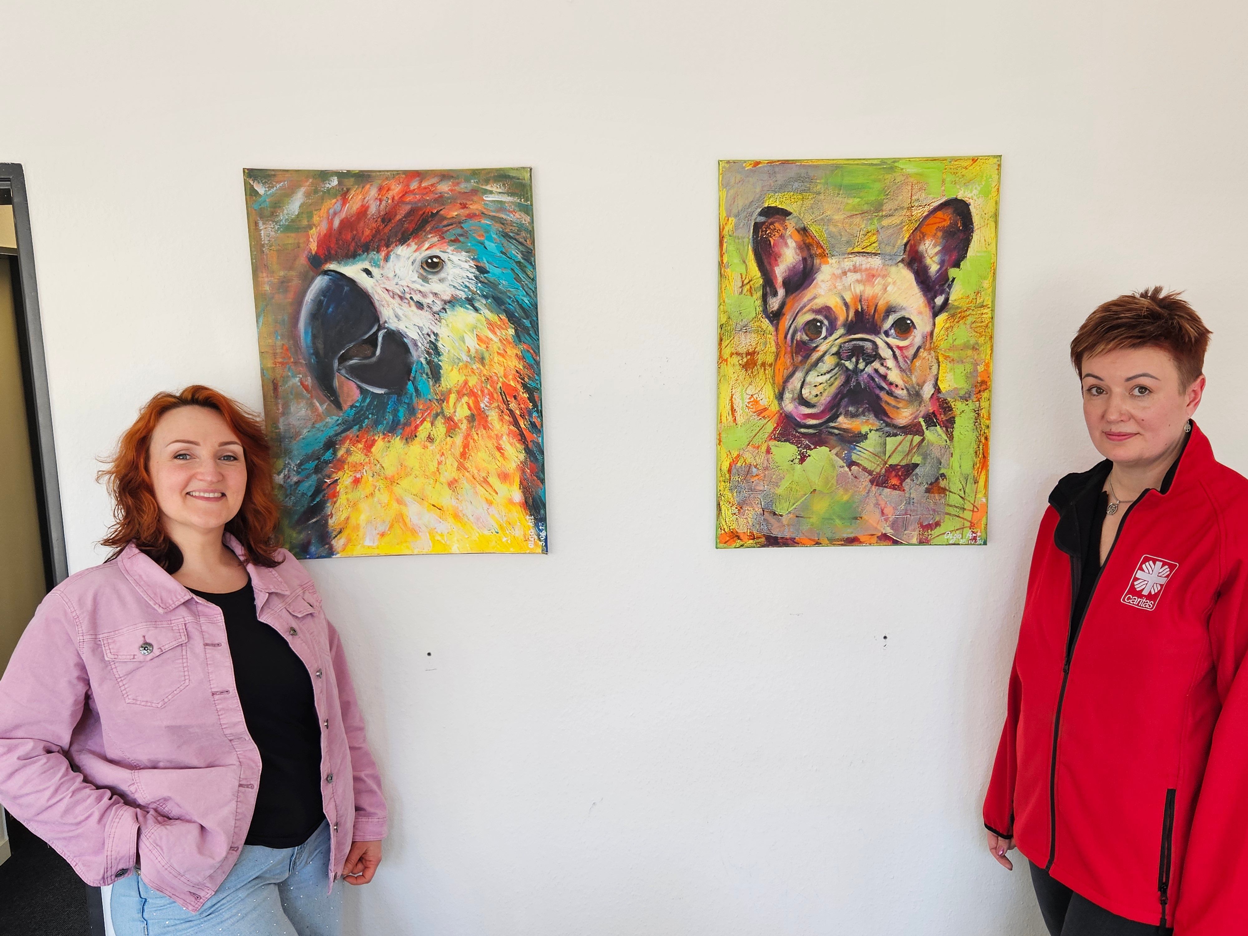Die beiden Frauen stehen vor einer Wand, an der zwei Tierbilder hängen.