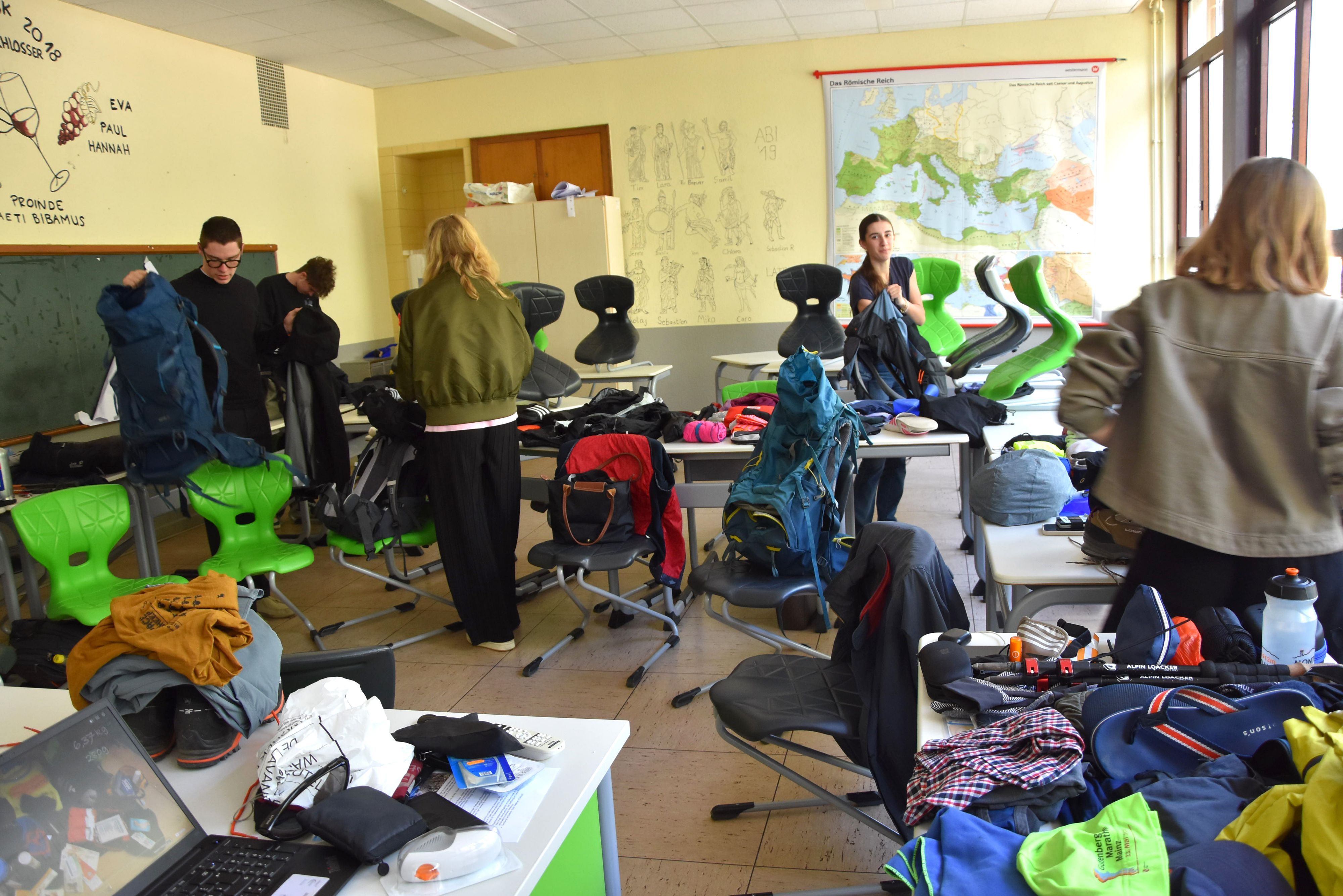 In einem Klassenzimmer packen Schülerinnen und Schüler Rucksäcke.