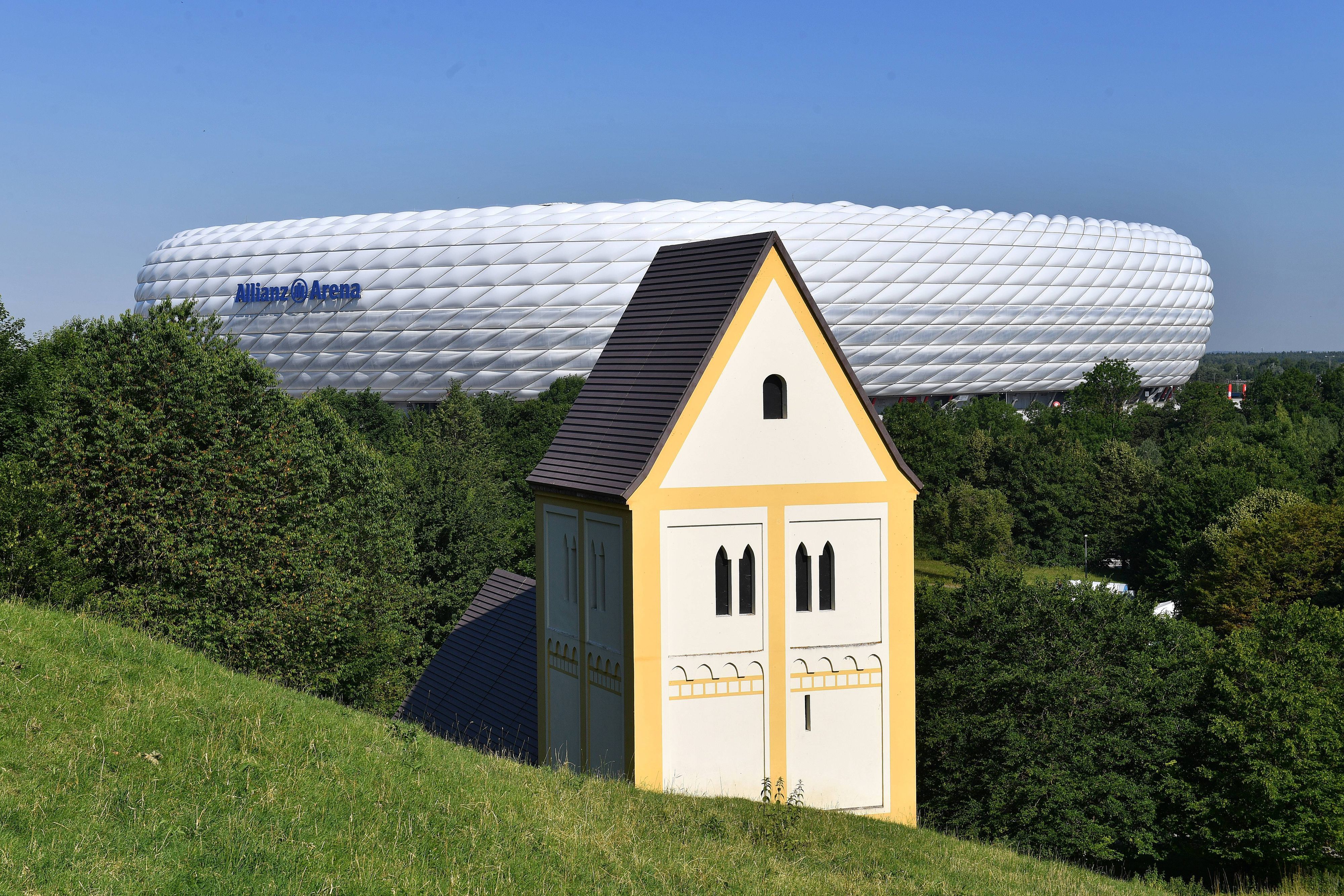 Die Nachbildung einer Kirche steht halb im Boden versunken vor einem Fußballstadion.