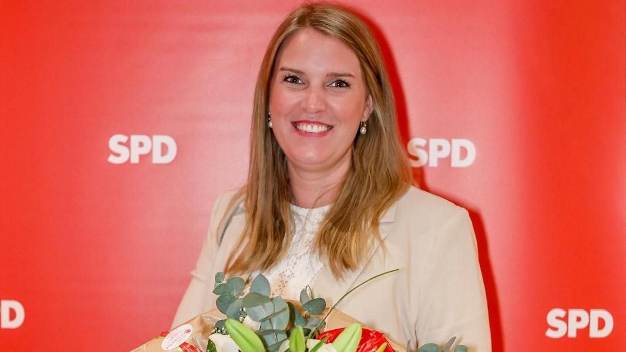 Das Bild zeigt Marie-Louise Knapp mit einem Strauß Blumen in der Hand vor einer roten Wand mit weißen SPD-Schriftzügen.
