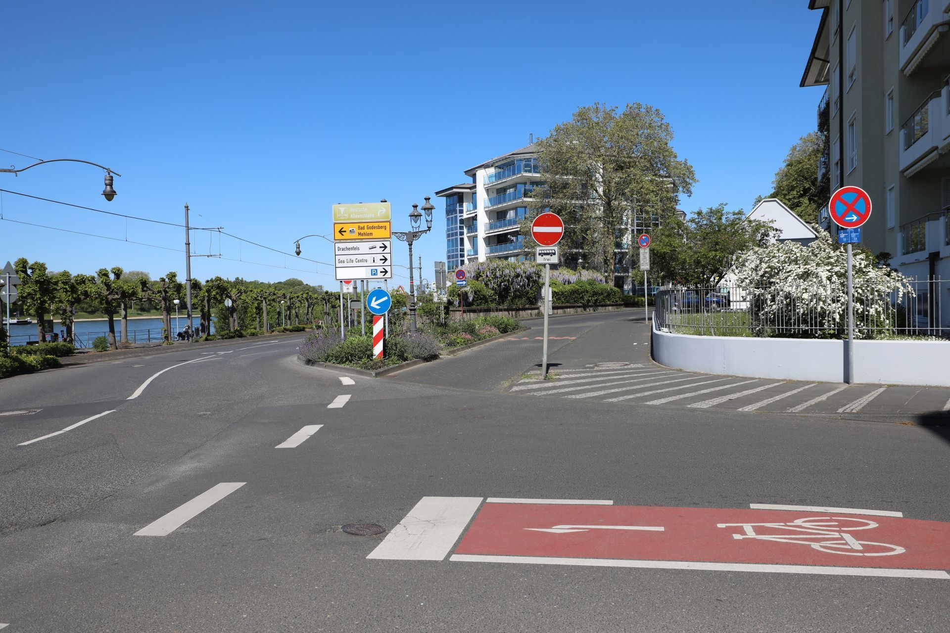 Eine Straßenkreuzung mit einer kurzen Extraspur für Busse, links im Hintergrund die Promenade am Rhein.