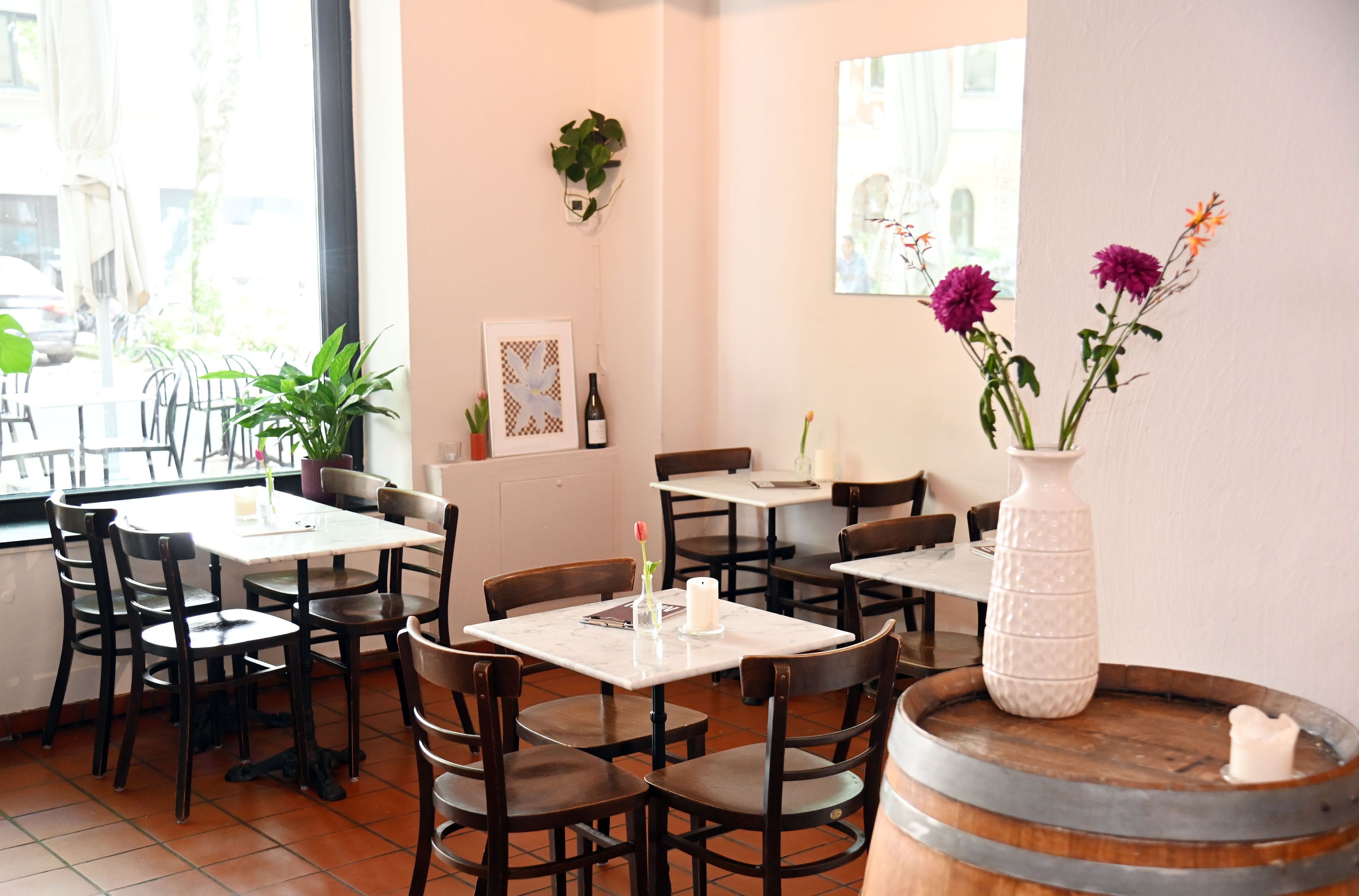 Der Gastraum der Bar mit kleinen Marmor-Tischen und Blumengesteck auf einem Weinfass.