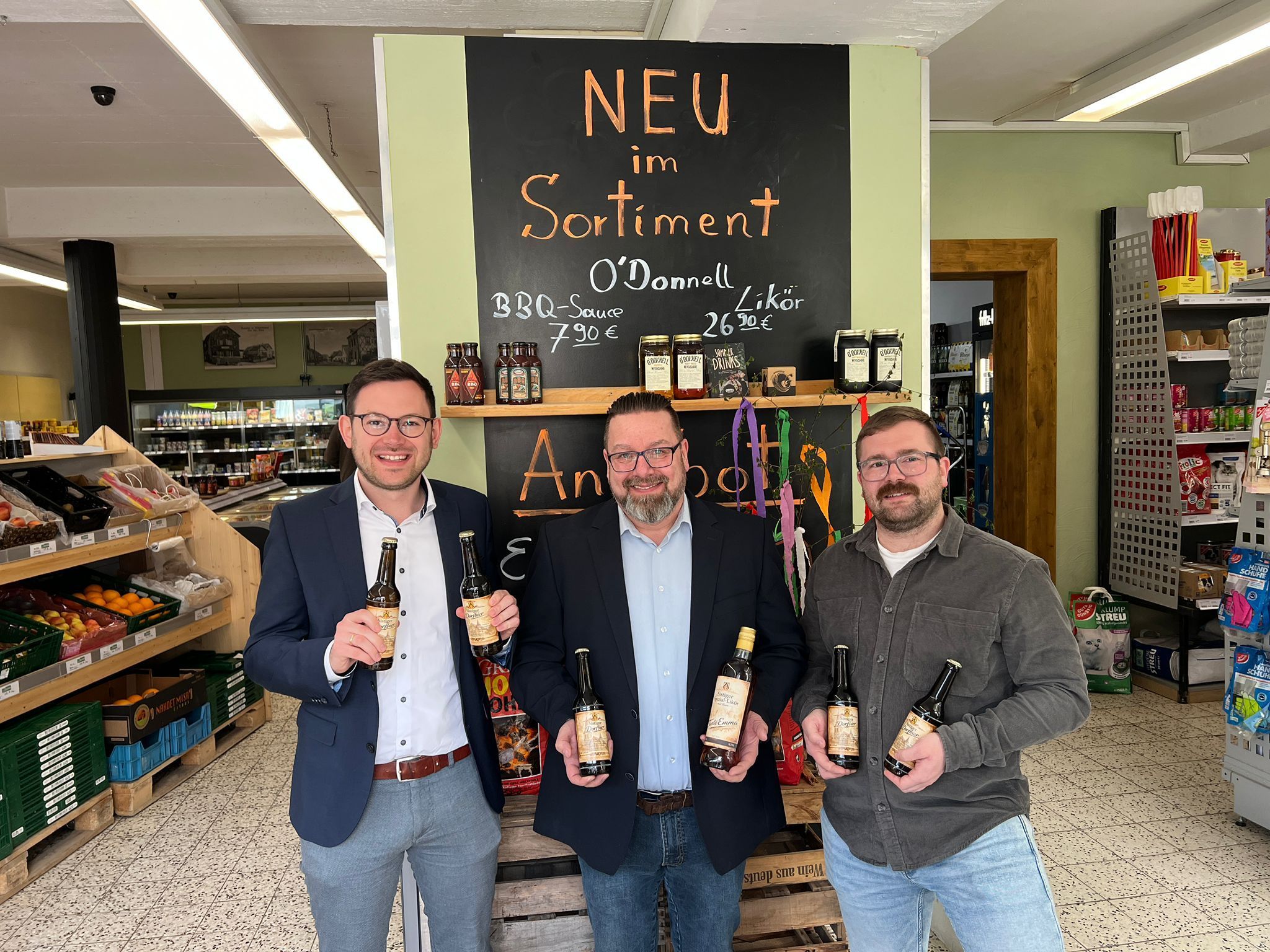 Drei Männer stehen im Verkaufsraum des Lädchen und präsentieren Bierflaschen.