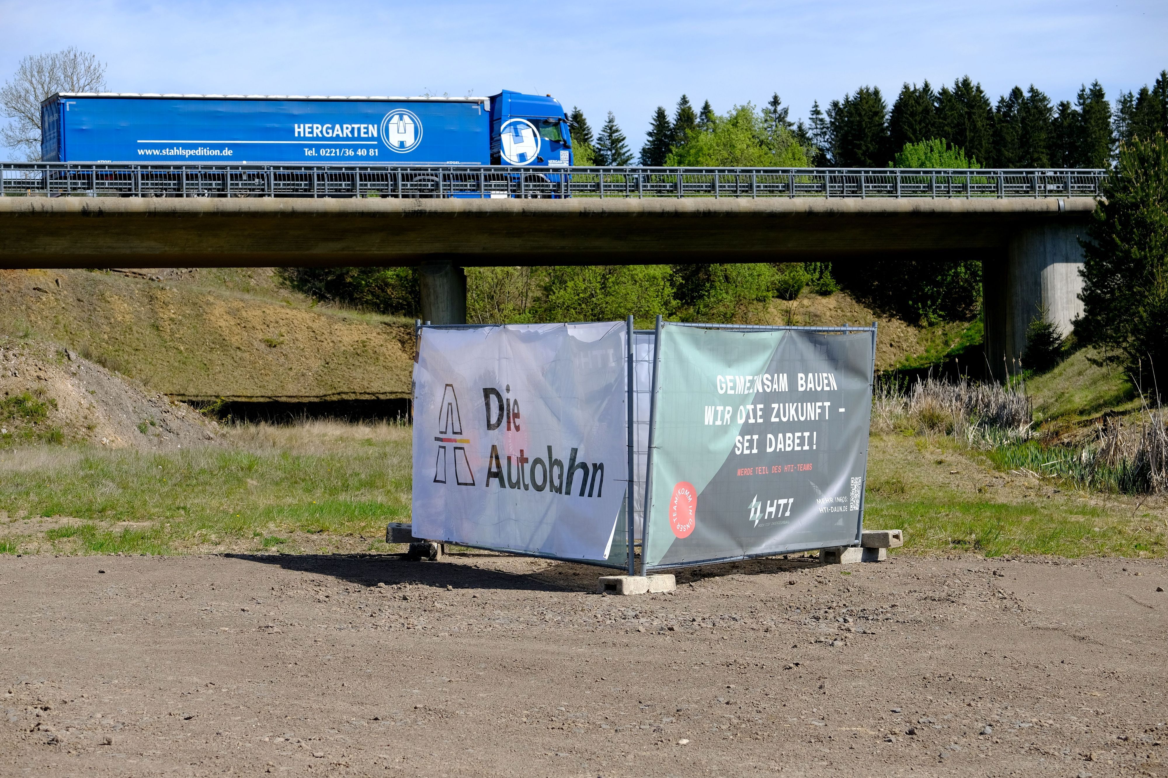 Beim Autobahnende der A1 in Rheinland-Pfalz fährt ein blauer LKW über eine Brücke, die über die künftige Autobahntrasse führt.