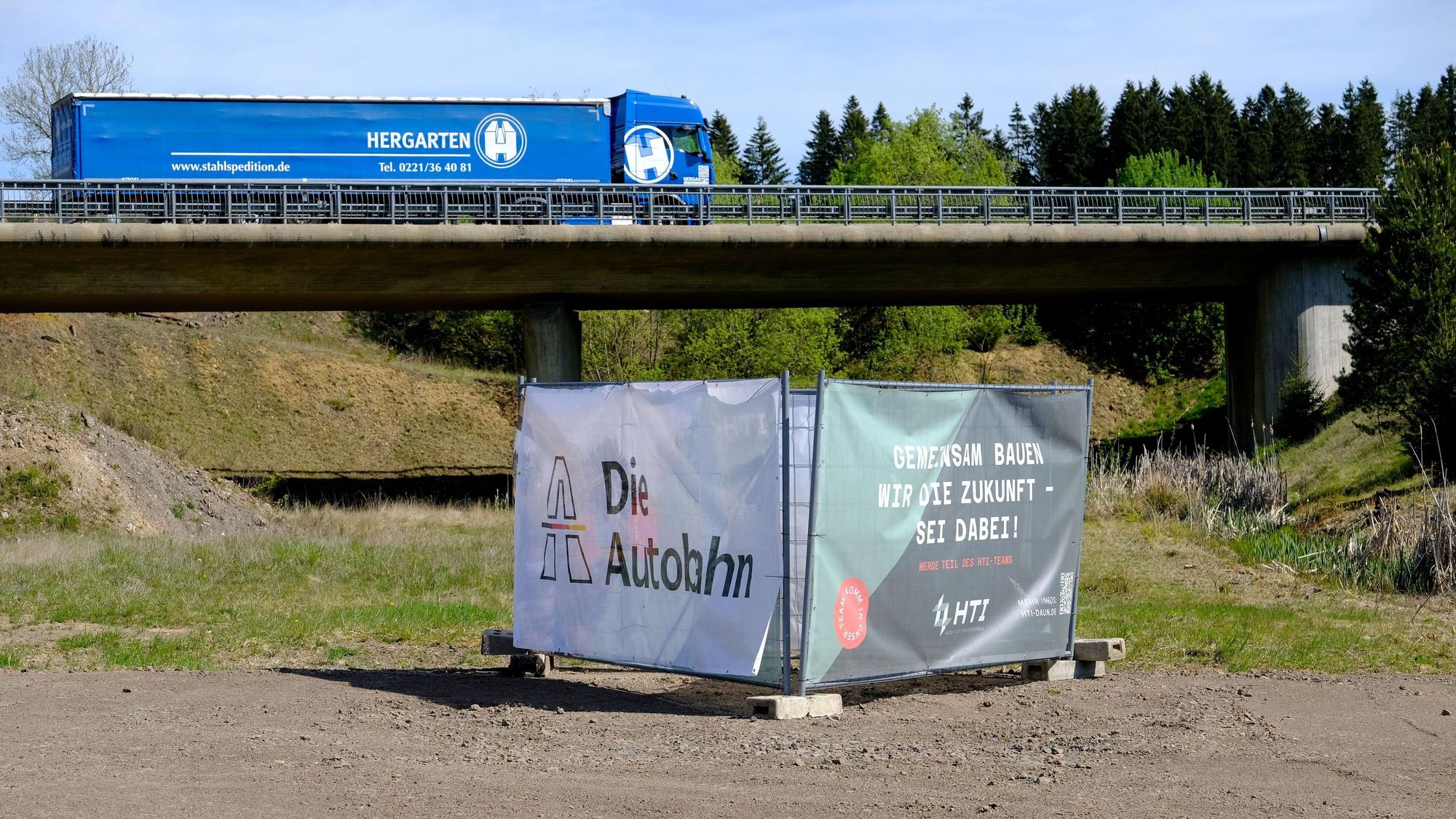 Beim Autobahnende der A1 in Rheinland-Pfalz fährt ein blauer LKW über eine Brücke, die über die künftige Autobahntrasse führt.