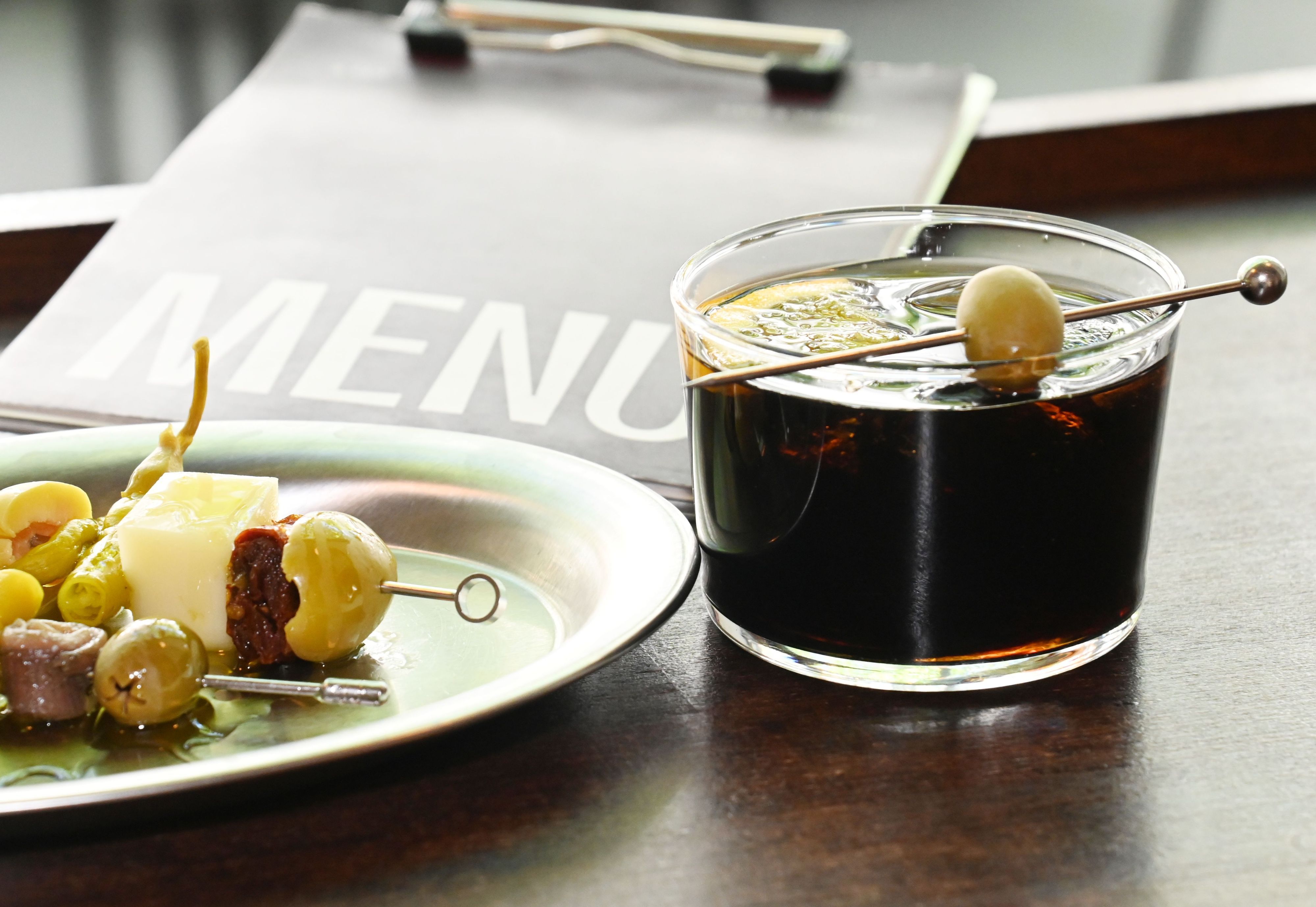 Ein Snack-Teller mit Spießchen und ein Cocktail mit Olive sind zu sehen.