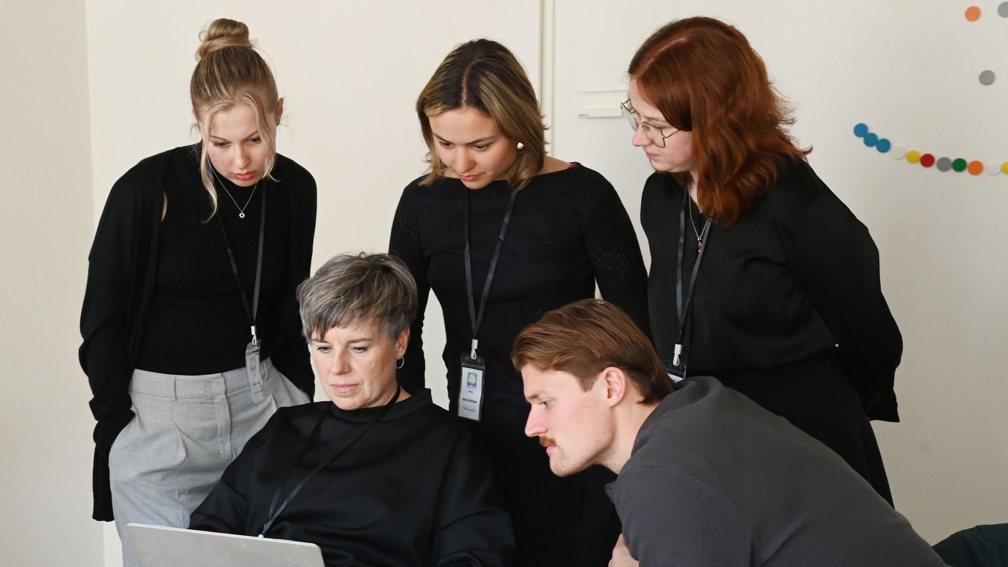 Fünf Personen schauen gemeinsam auf einen Laptop.