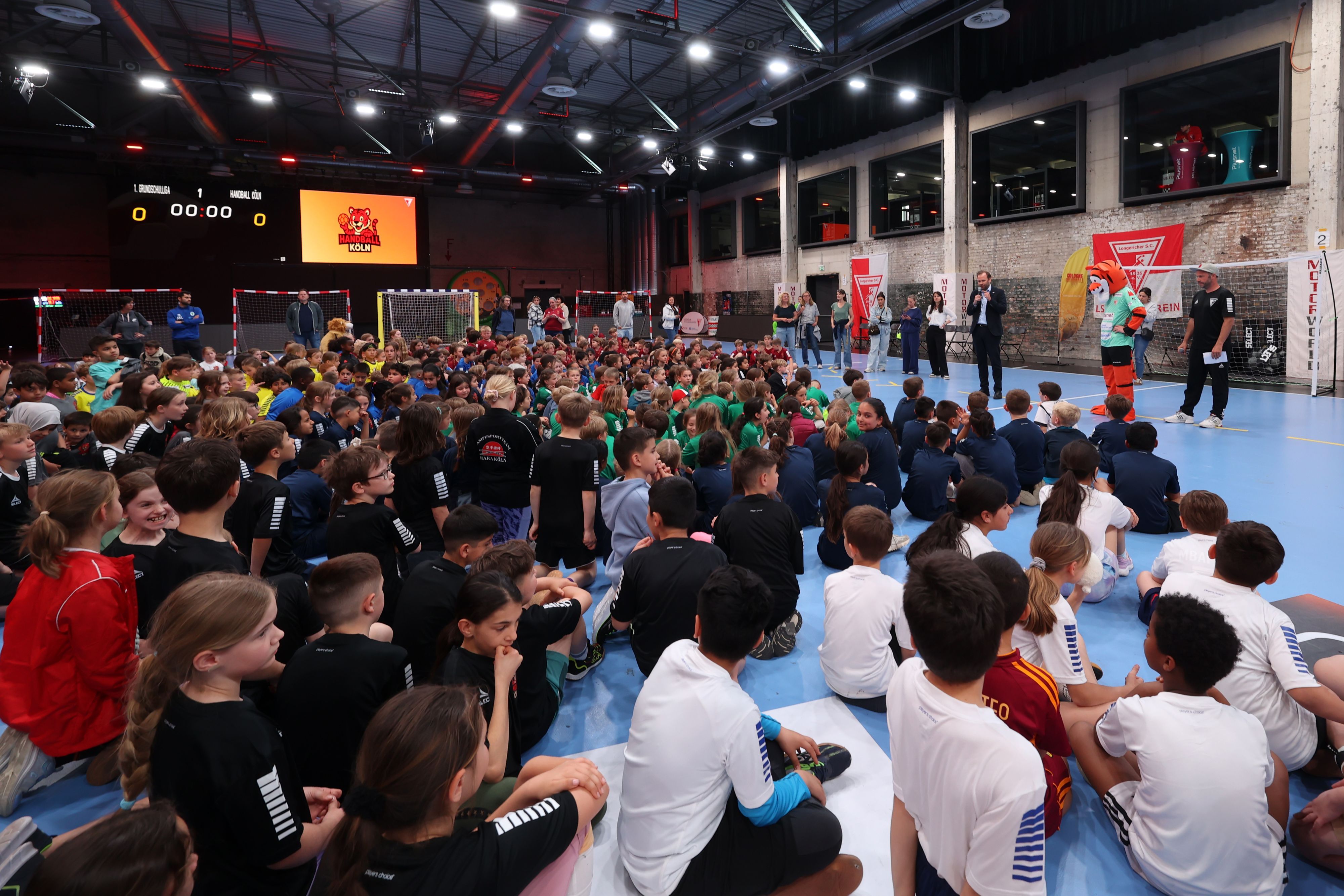 Grundschüler sitzen bei einer Siegerehrung eines Handball-Turniers auf dem Boden