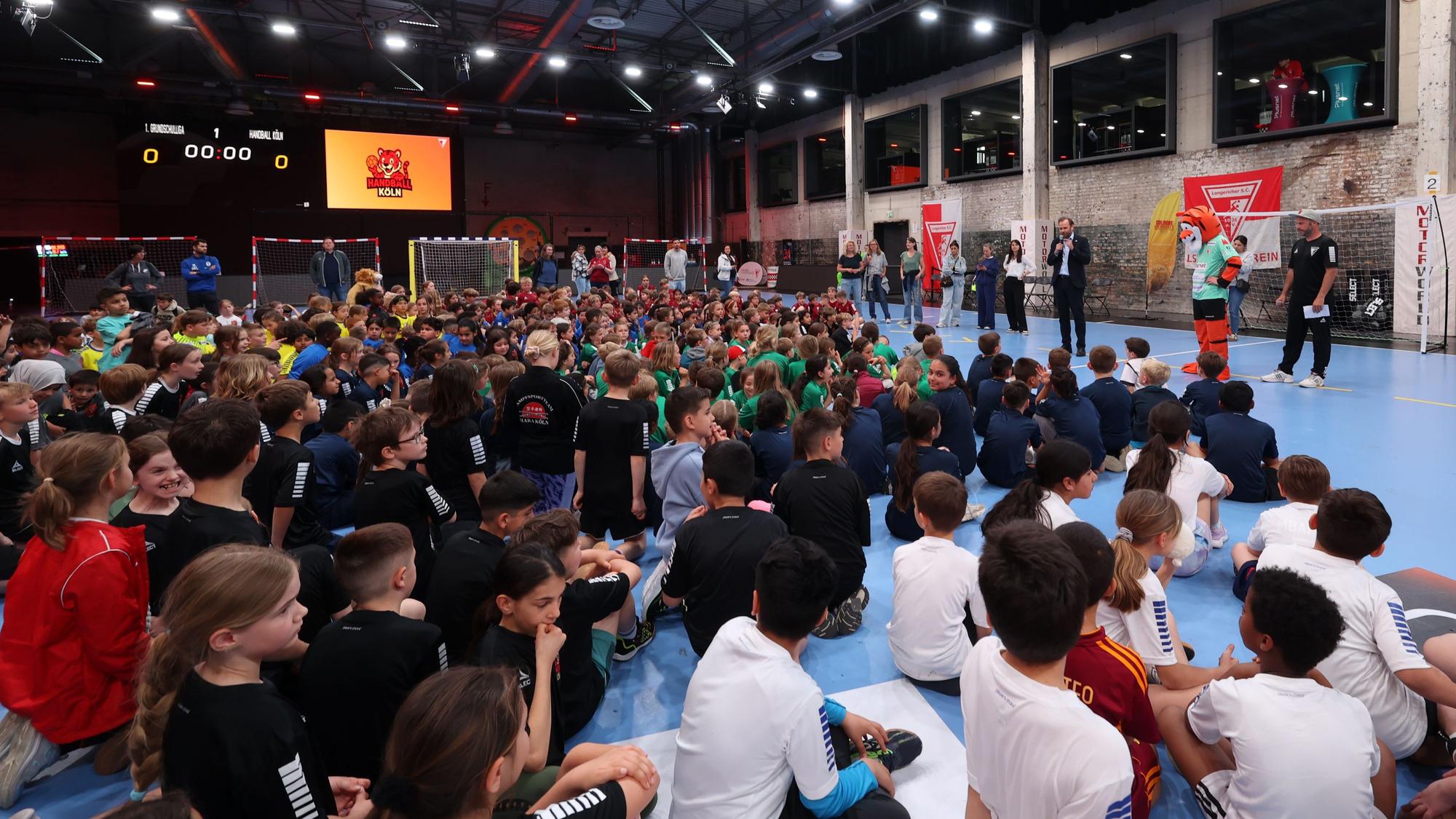 Grundschüler sitzen bei einer Siegerehrung eines Handball-Turniers auf dem Boden