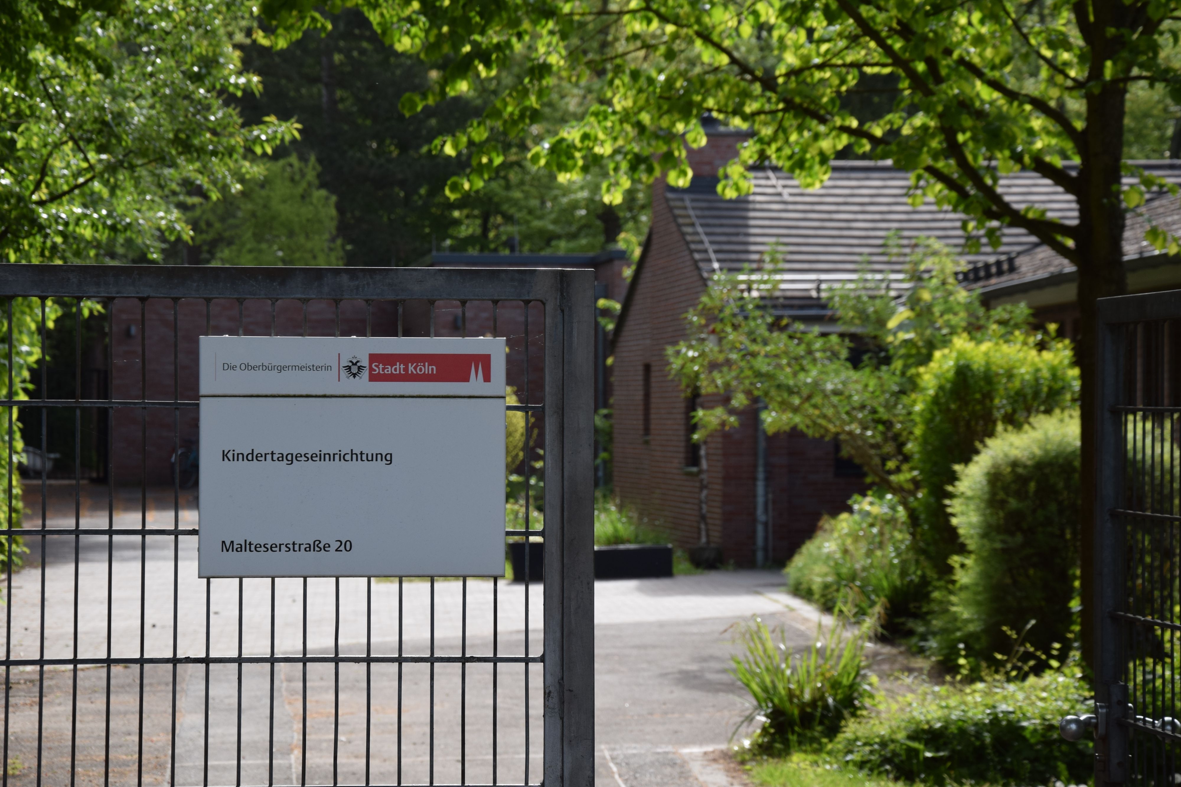 An einem Gittertor hängt ein Schild: Kindertageseinrichtung Malteserstraße 20.