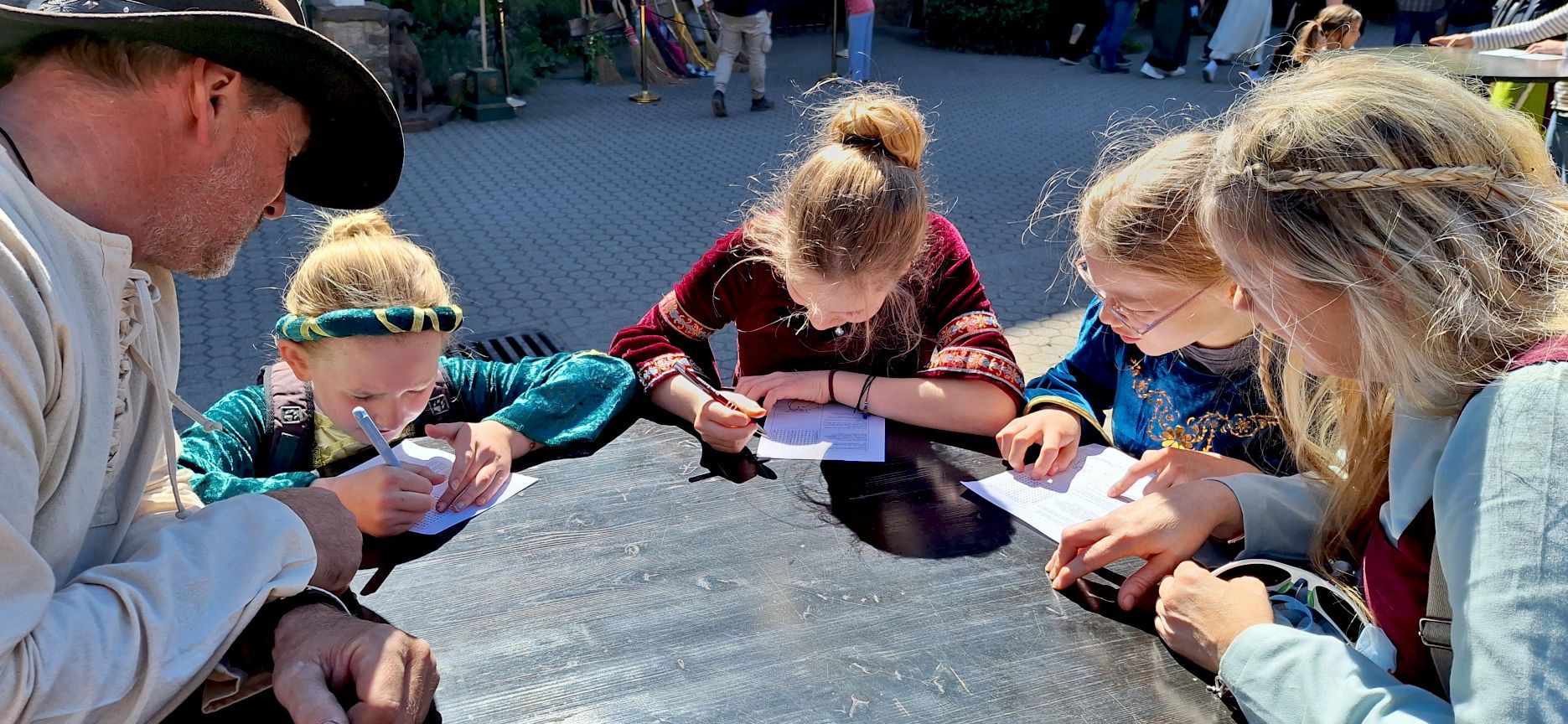 Die Familie sitzt rund um einen Tisch. Die Kinder füllen Fragebogen aus.