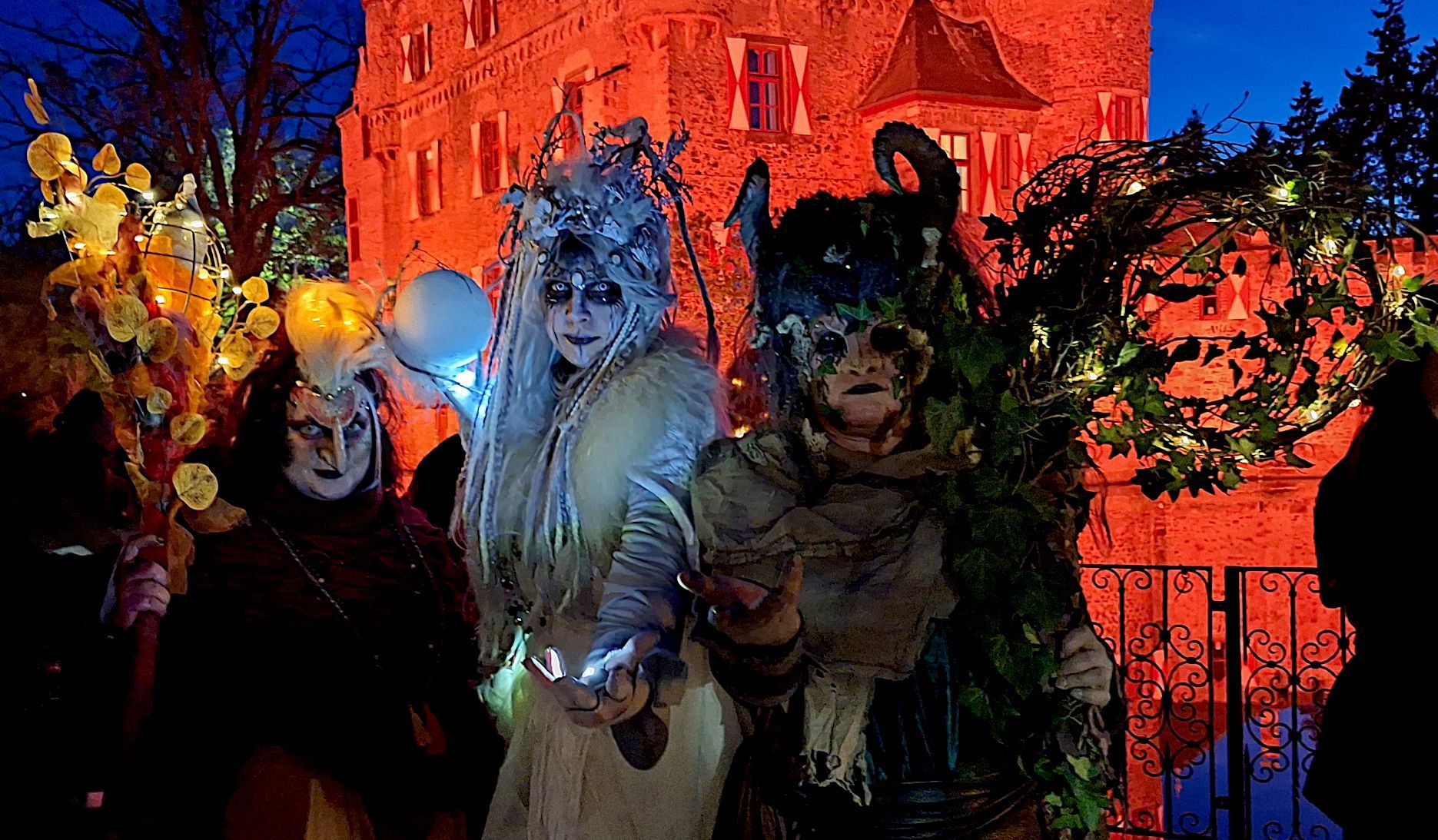 Die drei kostümierten Hexen in aufwendigen Kostümen vor der orange angestrahlten Burg.