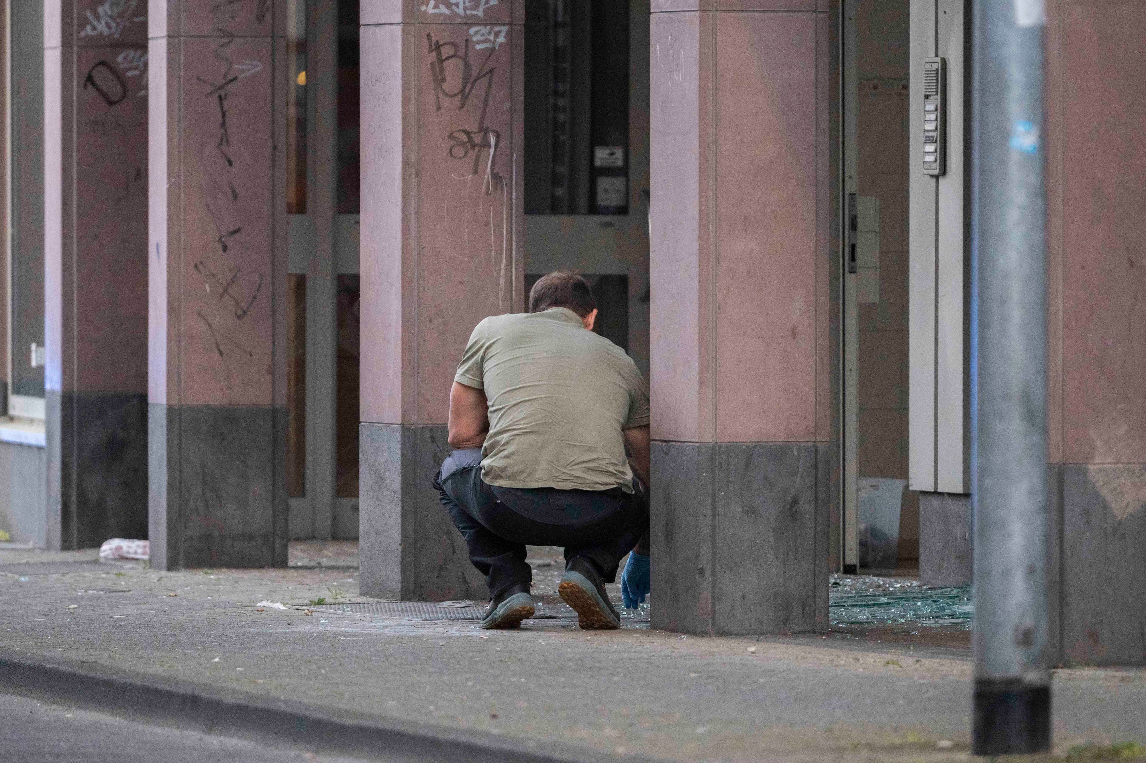 Das Bild zeigt einen Beamten, der mit Einweghandschuhen in Glassplittern nach Spuren sucht.
