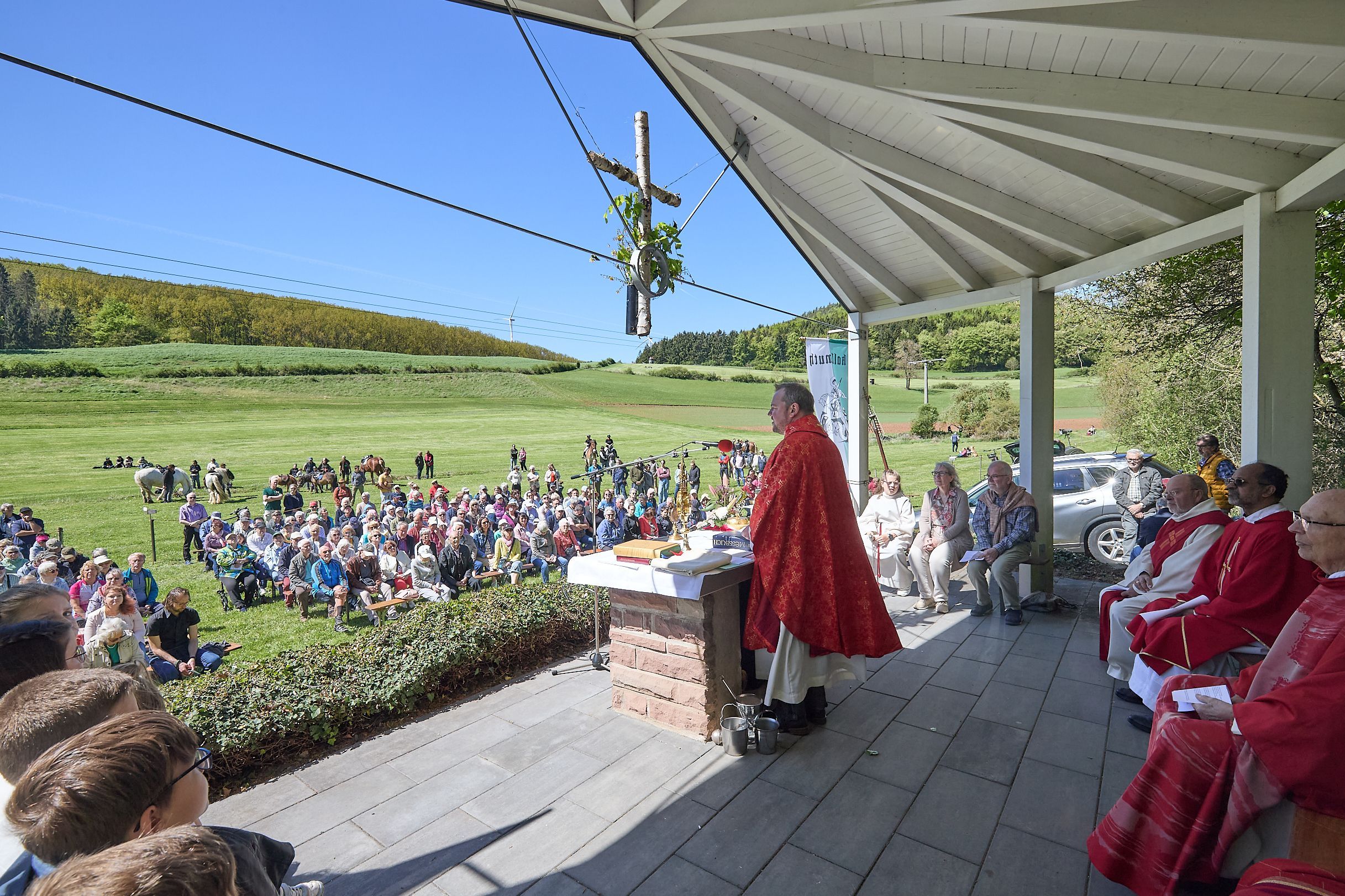 Am Altar vor der Festwiese steht der Pfarrer, die übrigen Kirchenvertreter sitzen hinter ihm. Auf der Wiese sitzen zahlreiche Gottesdienstteilnehmer.