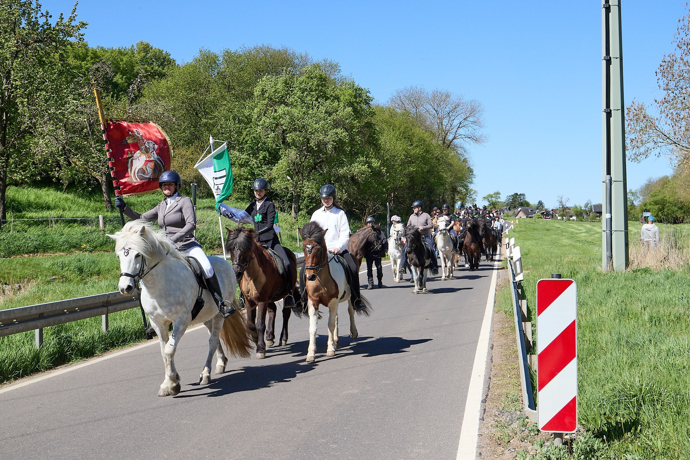 Die Prozession der Reiter zieht über eine Straße. Allen voran die berittenen Fahnenträger.