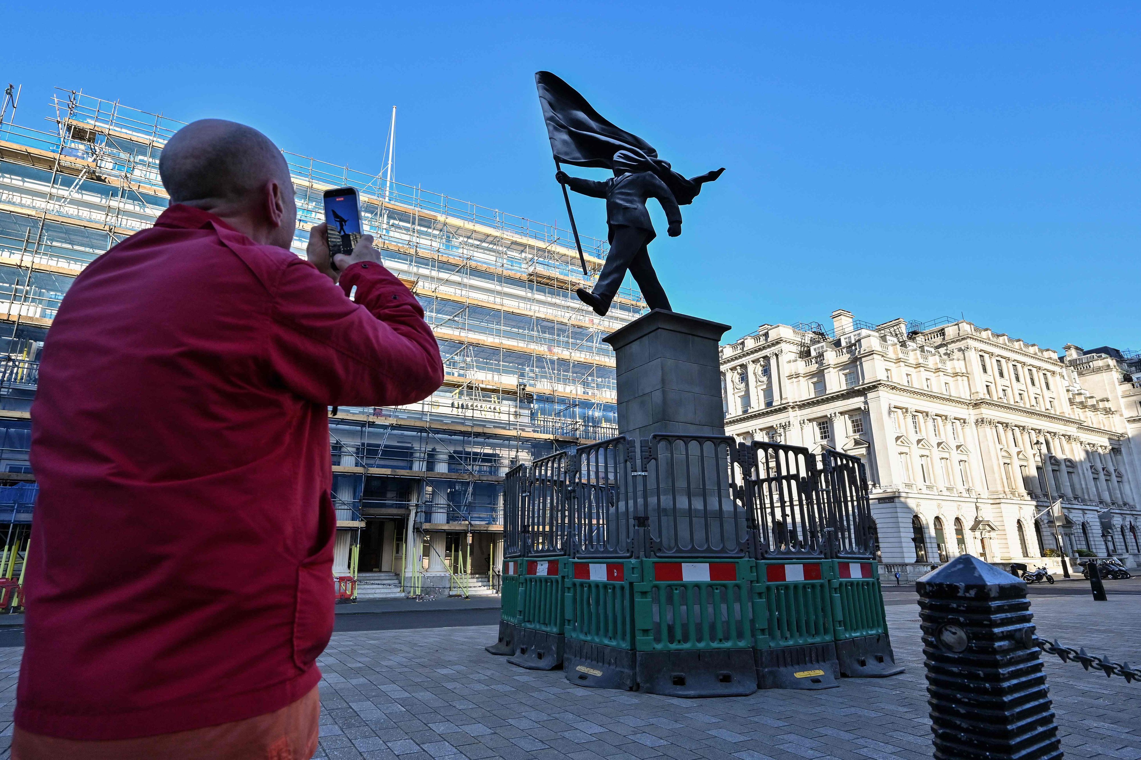 Am Waterloo Place im Zentrum Londons steht eine Statue, die einen Mann zeigt, der eine Flagge hält, die sein Gesicht verdeckt, und die am Sockel mit „Banksy“ unterzeichnet ist.
