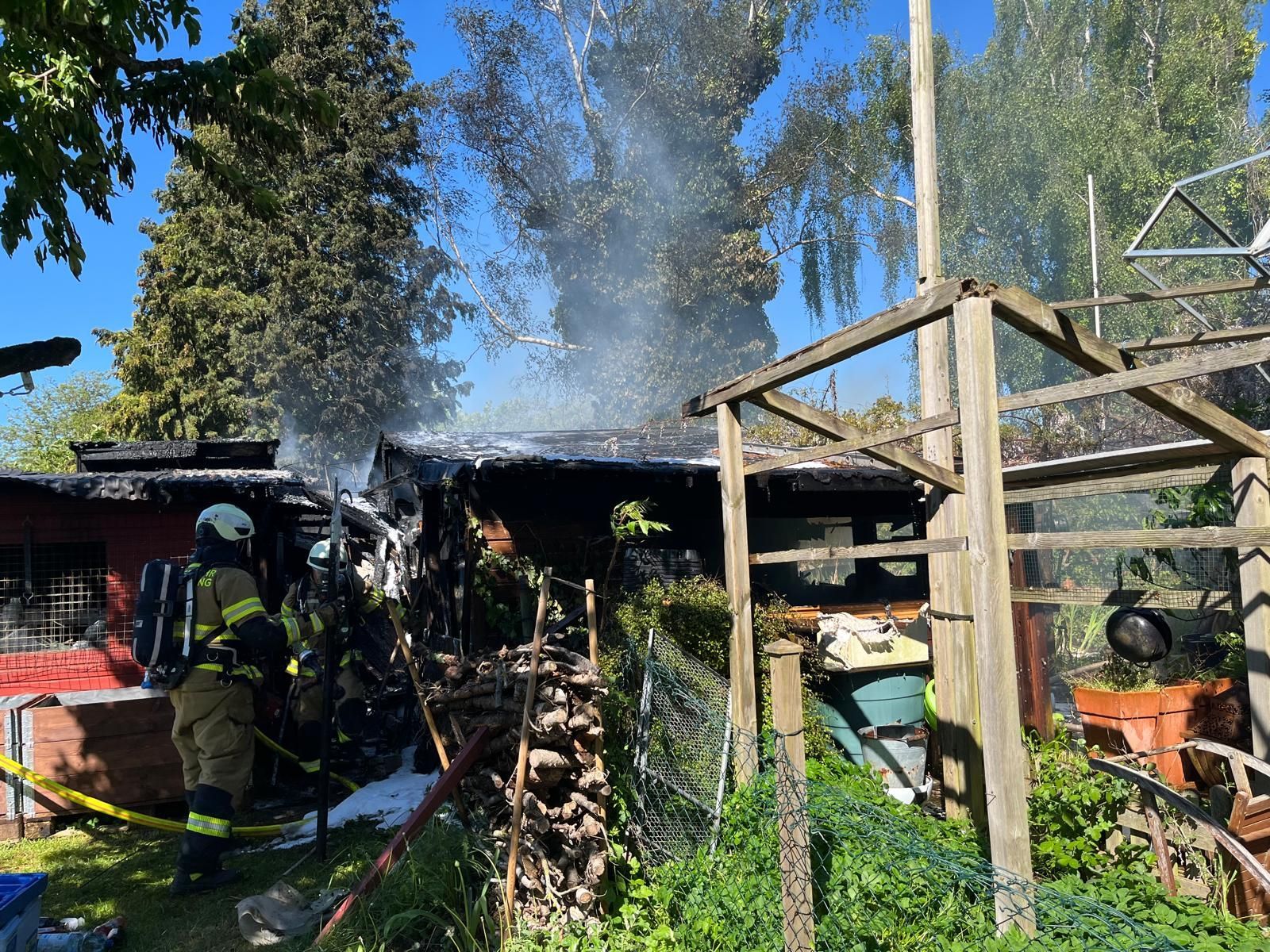 Das Bild zeigt die Feuerwehr, die ein Feuer in einer Gartenhütte löscht.