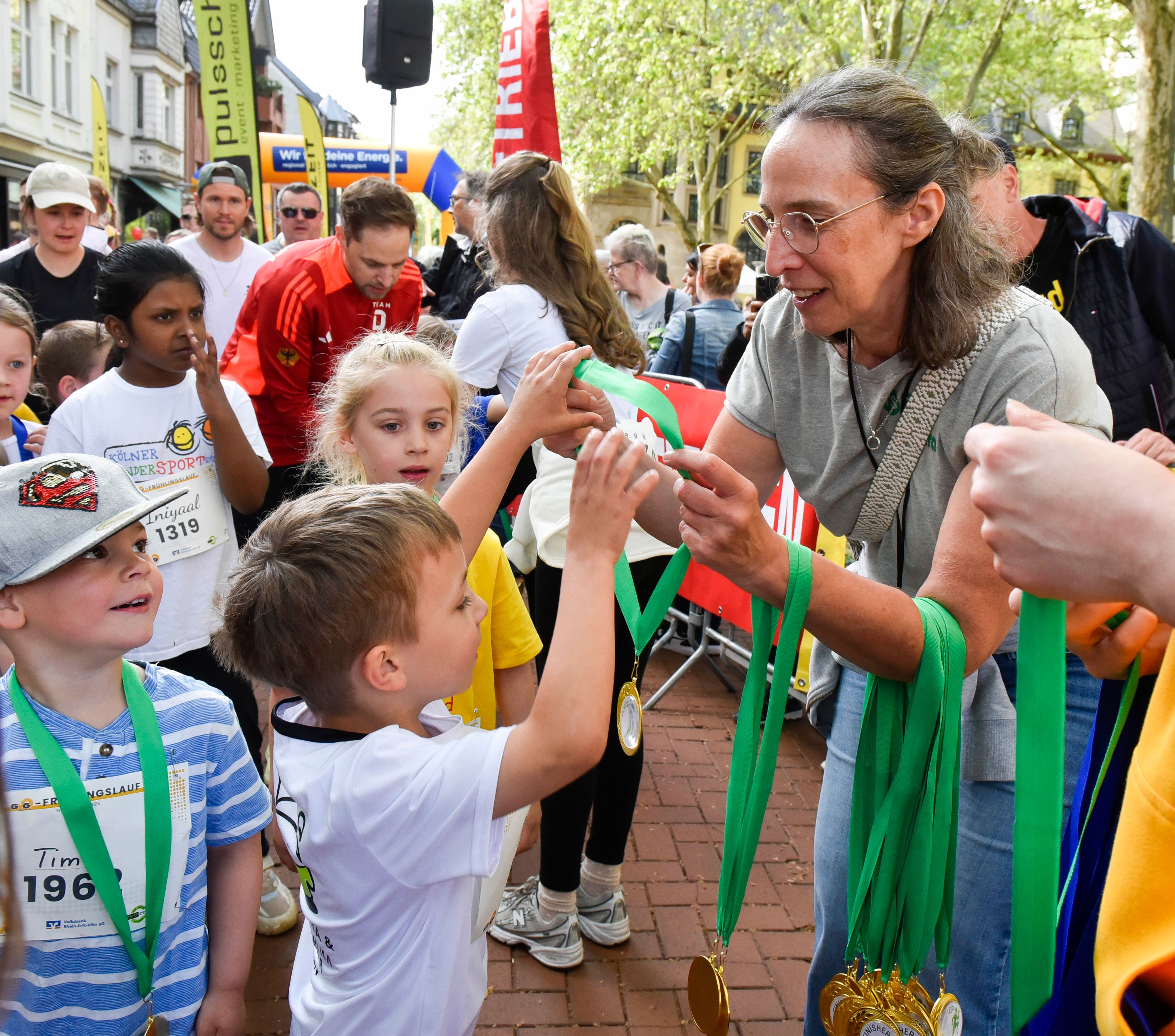 Auf dem Bild sind Kinder zu sehen, die von einer Frau Medaillen überreicht bekommen.