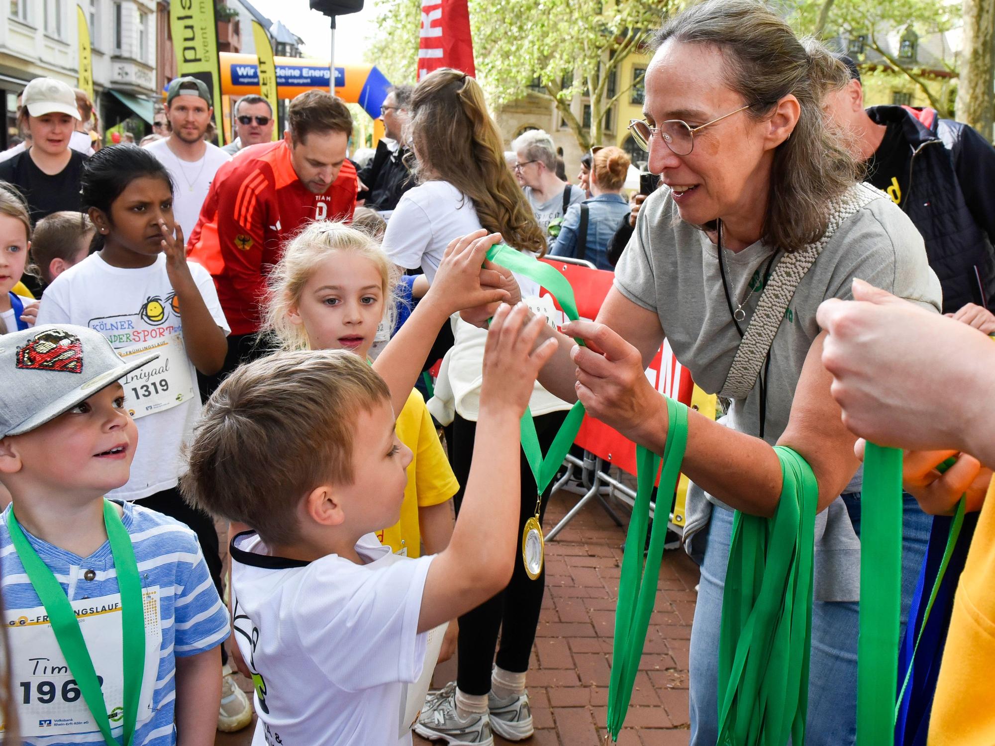 Auf dem Bild sind Kinder zu sehen, die von einer Frau Medaillen überreicht bekommen.