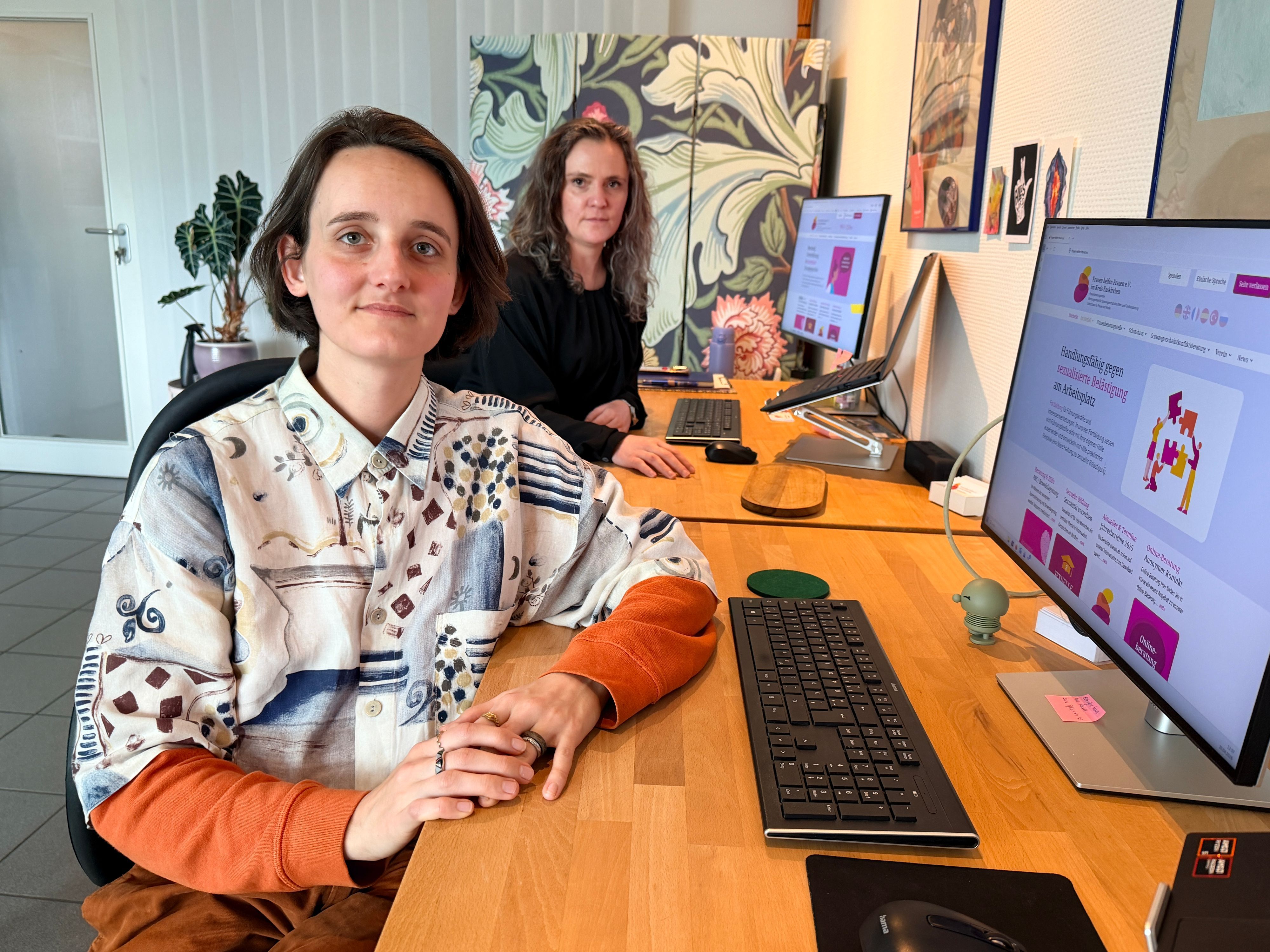 Die beiden Sozialarbeiterinnen sitzen an Schreibtischen vor den PCs.