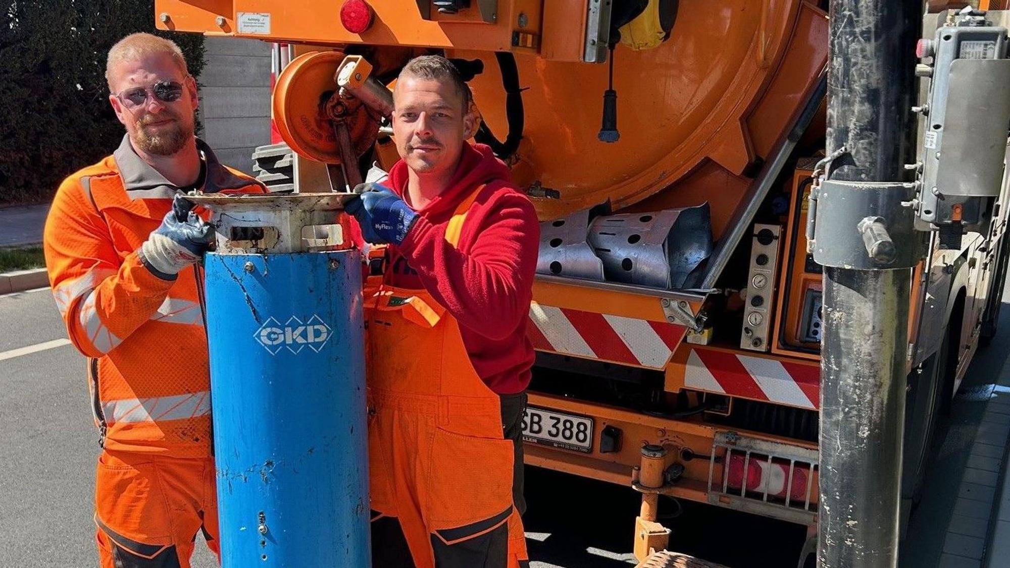 Zwei Männer halten eine großen blauen zylinderförmigen Gegenstand in die Kamera.