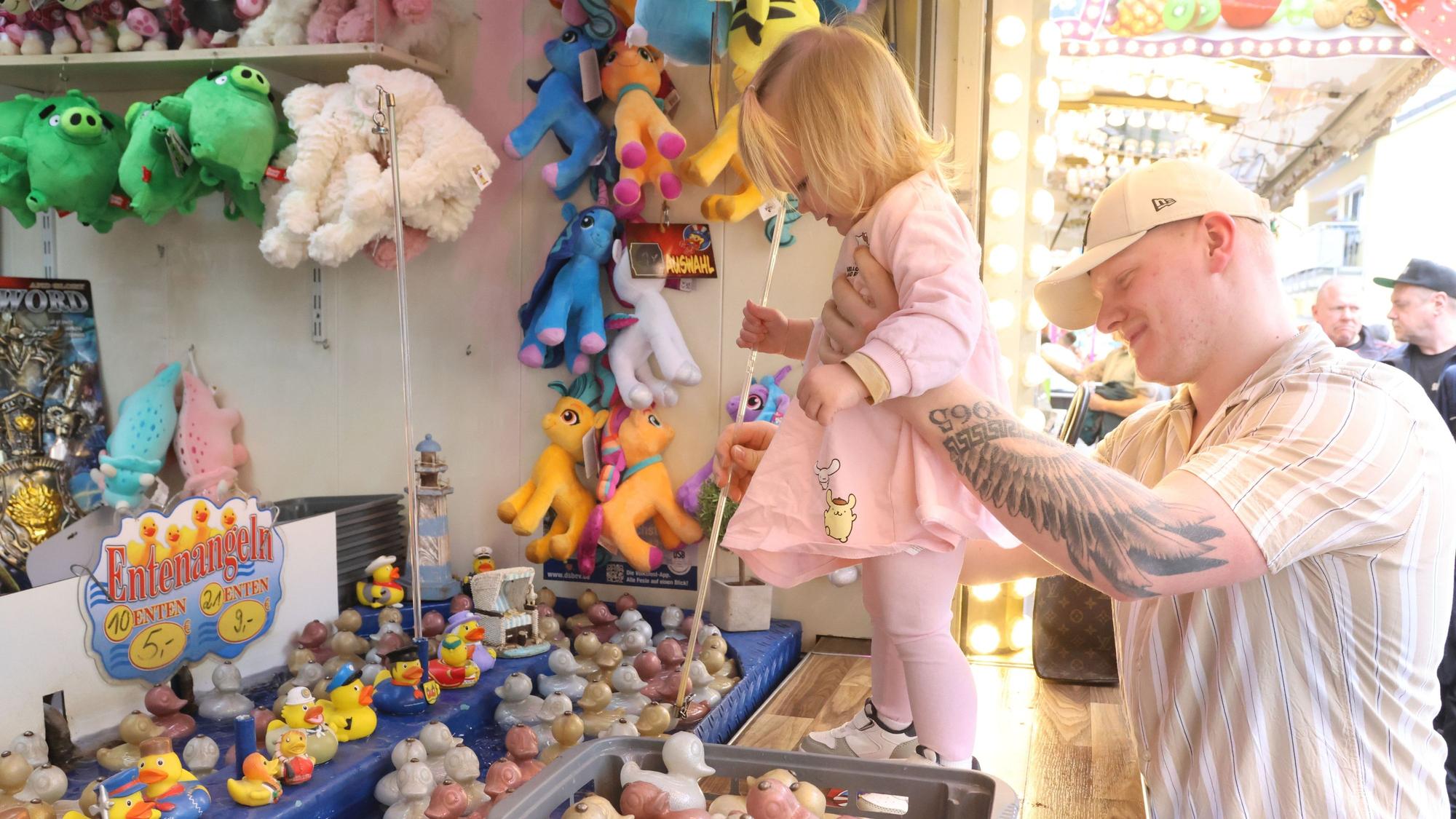 Ein kleines Mädchen angelt mithilfe seines Vaters Entchen auf einer Maikirmes.