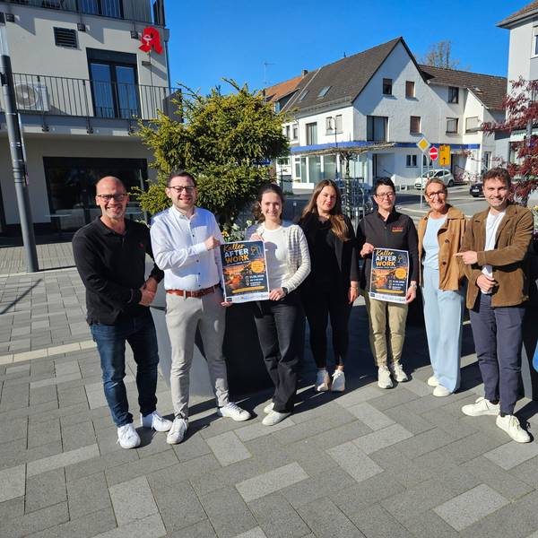 Vier Männer und vier Frauen stehen auf dem Bahnhofsvorplatz nebeneinander und präsentieren zwei Plakate.