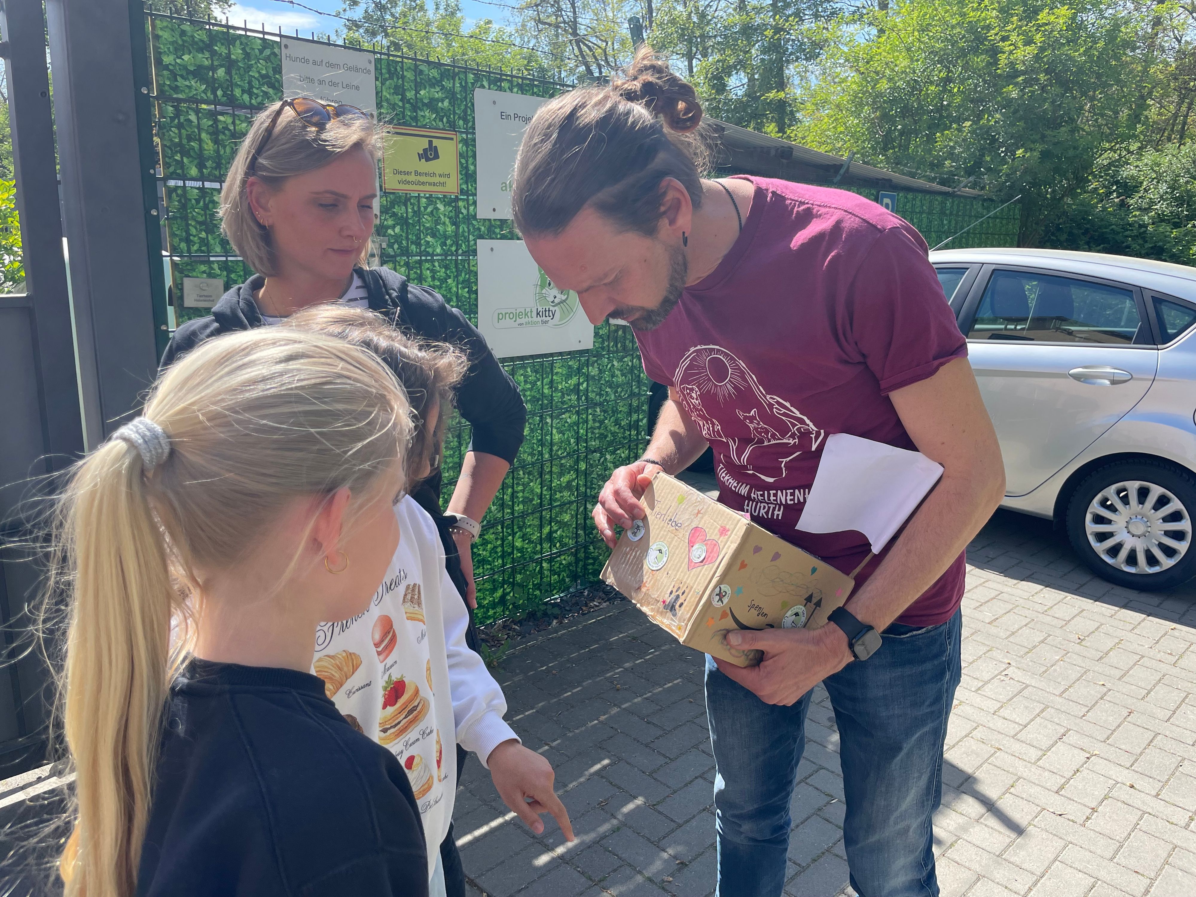 Das Foto zeigt einen Mann mit einer Spendenbox, daneben eine junge Frau und ein Mädchen.