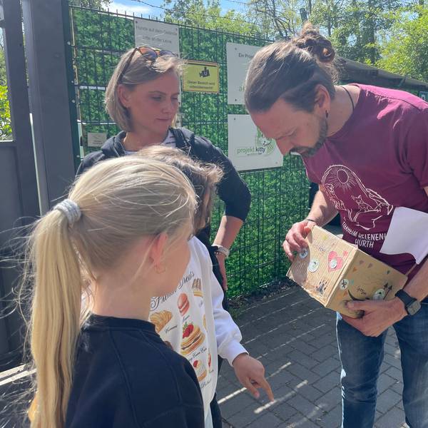 Das Foto zeigt einen Mann mit einer Spendenbox, daneben eine junge Frau und ein Mädchen.