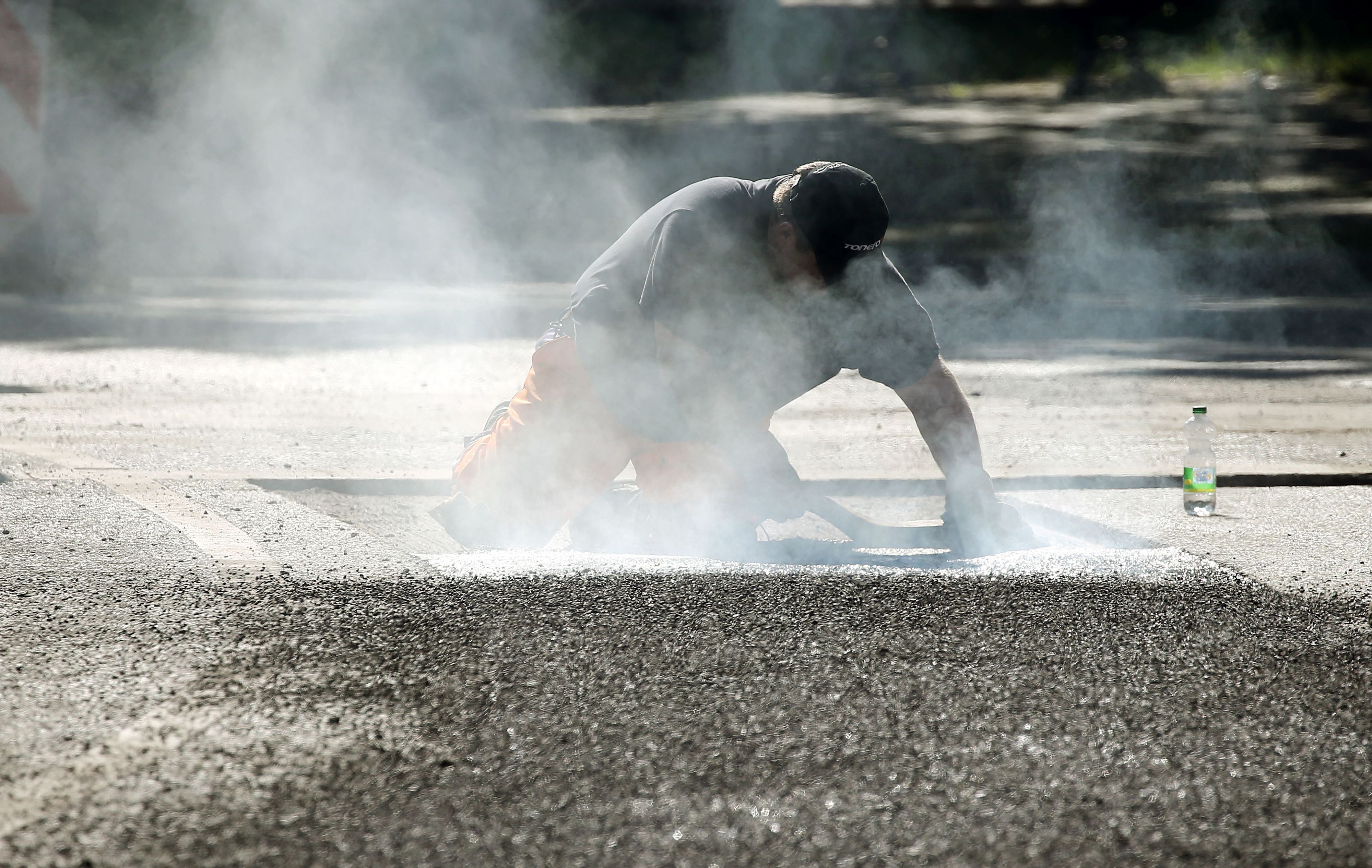 Ein Straßenbauarbeiter repariert mit 240-Grad-heißem Bitumen Schäden am Straßenbelag.
