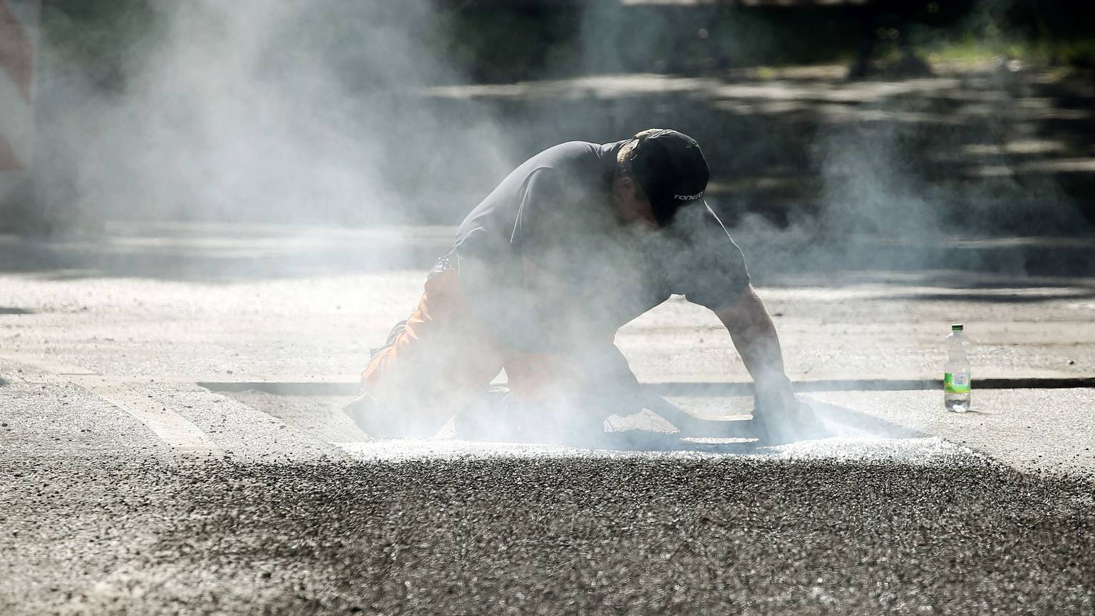 Ein Straßenbauarbeiter repariert mit 240-Grad-heißem Bitumen Schäden am Straßenbelag.