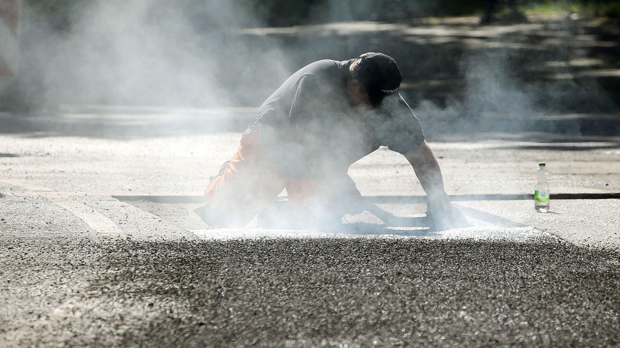 Ein Straßenbauarbeiter repariert mit 240-Grad-heißem Bitumen Schäden am Straßenbelag.
