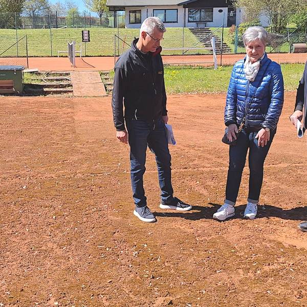 Die drei personen stehen auf einem Tennisplatz und betrachten den rötlichen Belag.