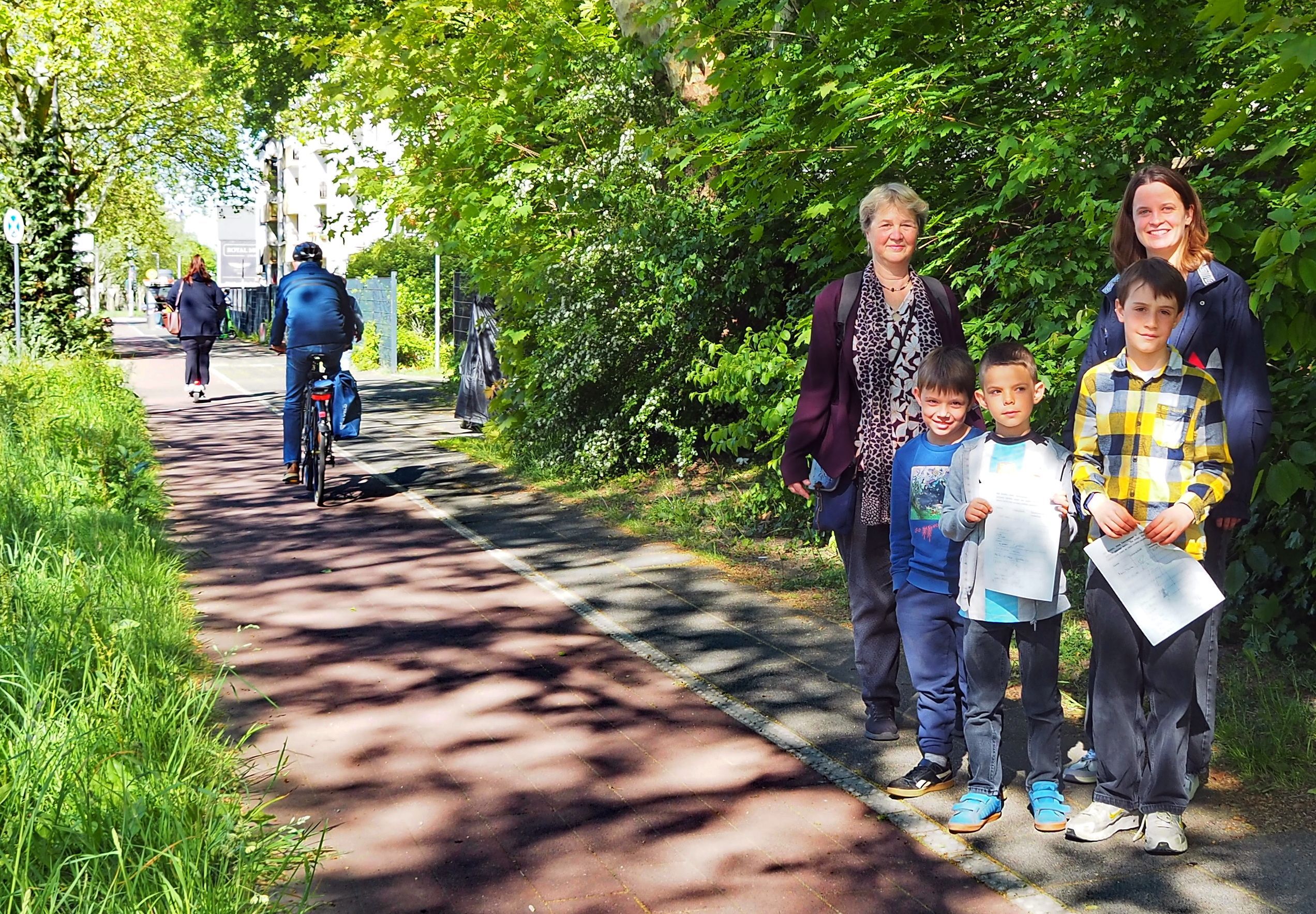 Drei Kinder und zwei Frauen stehen am Rand eines Radwegs.