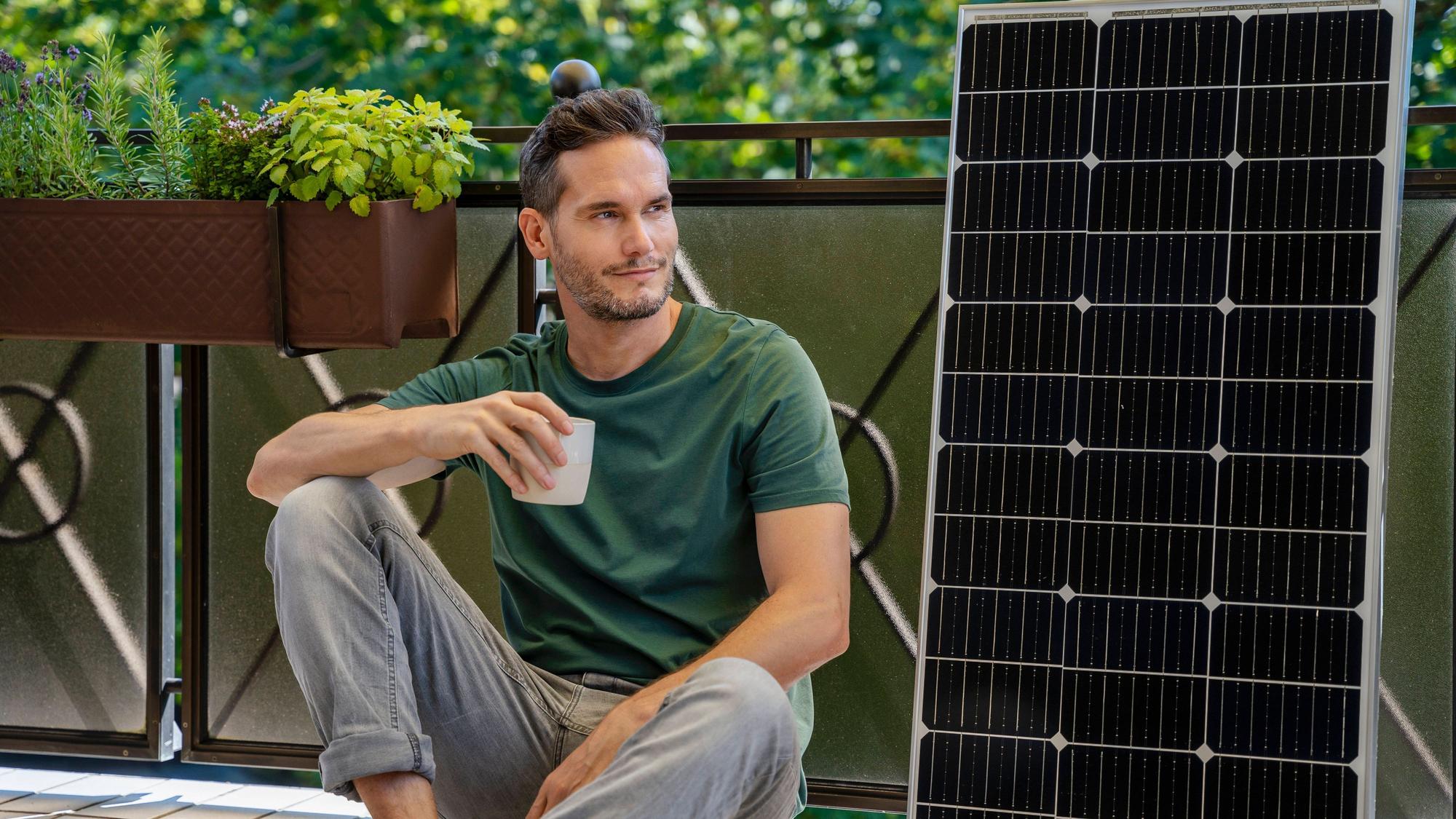 Mann mit Kaffee, Solarmodul und Pflanzen auf Balkon