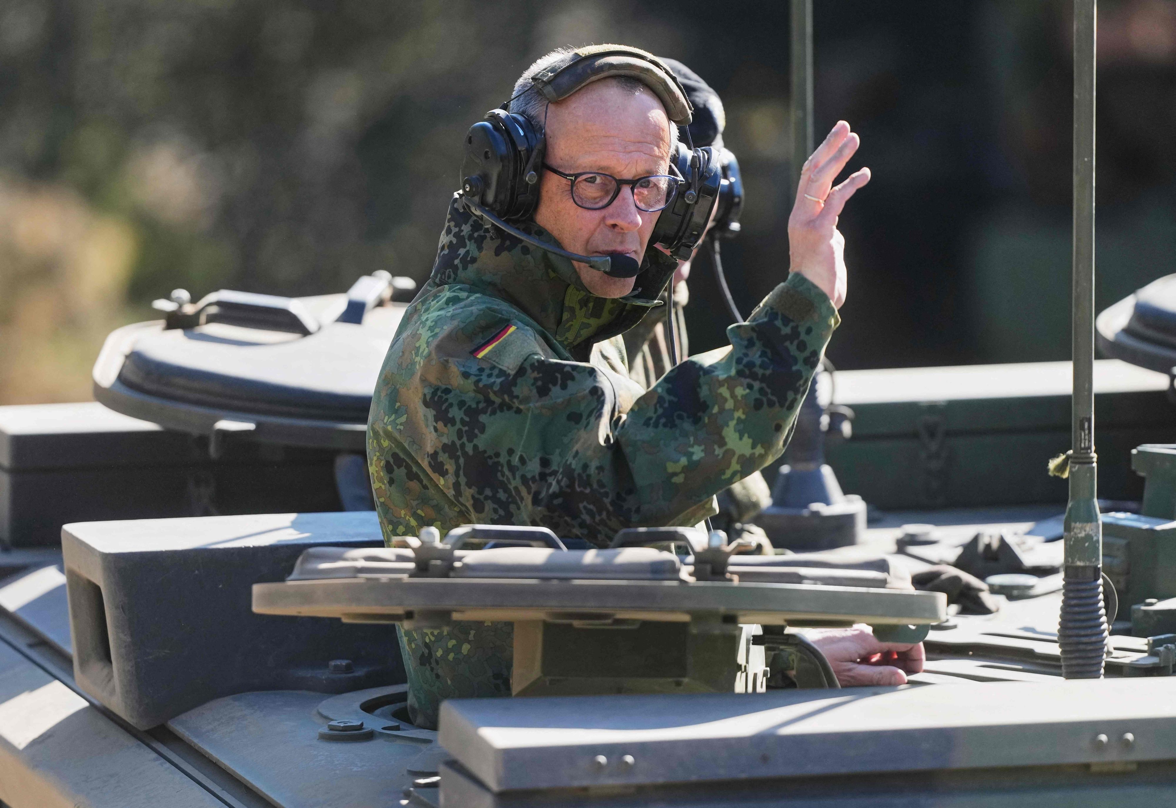 Bundeskanzler Friedrich Merz winkt aus einem Panzer.