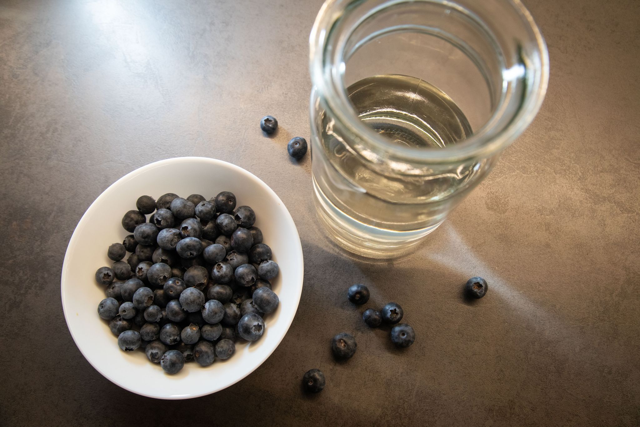 Blaubeeren liegen in einer Schale neben einem Glas Wasser