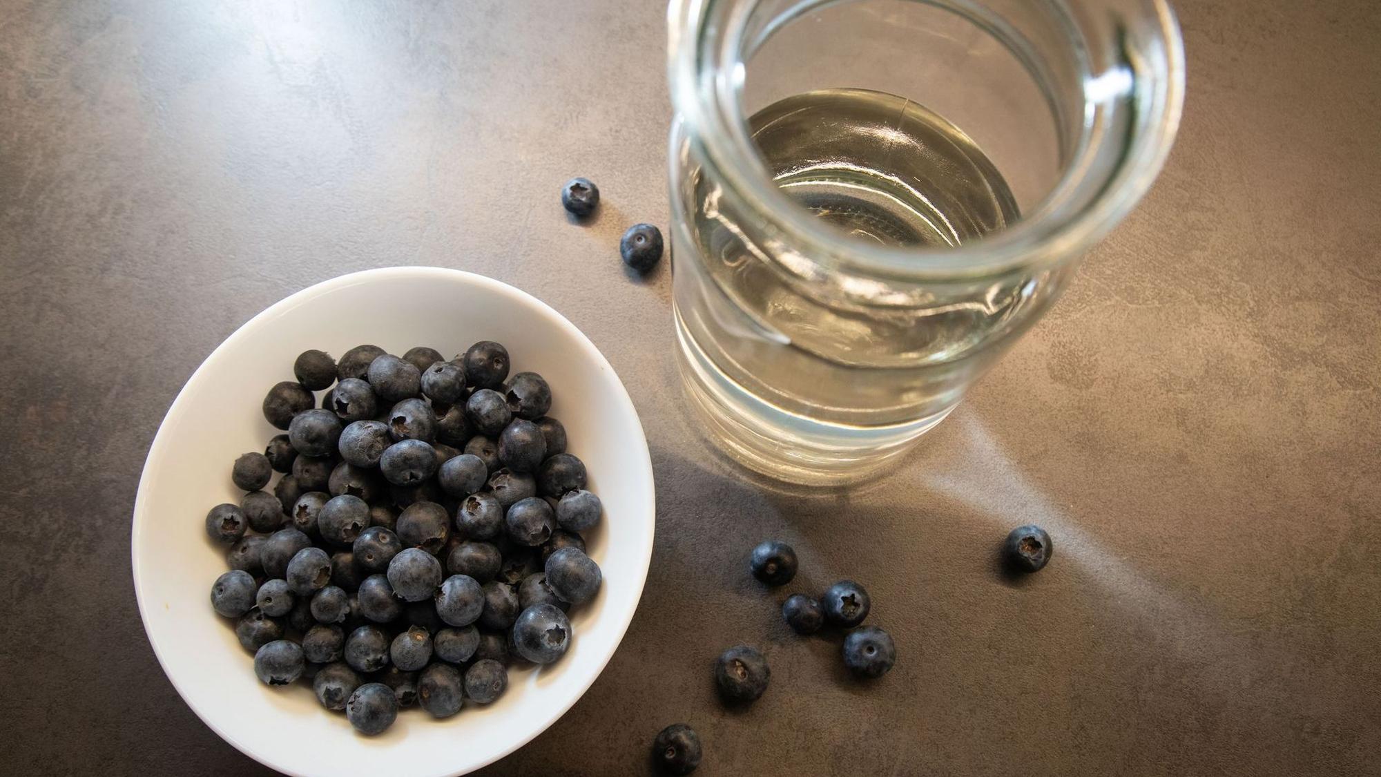 Blaubeeren liegen in einer Schale neben einem Glas Wasser