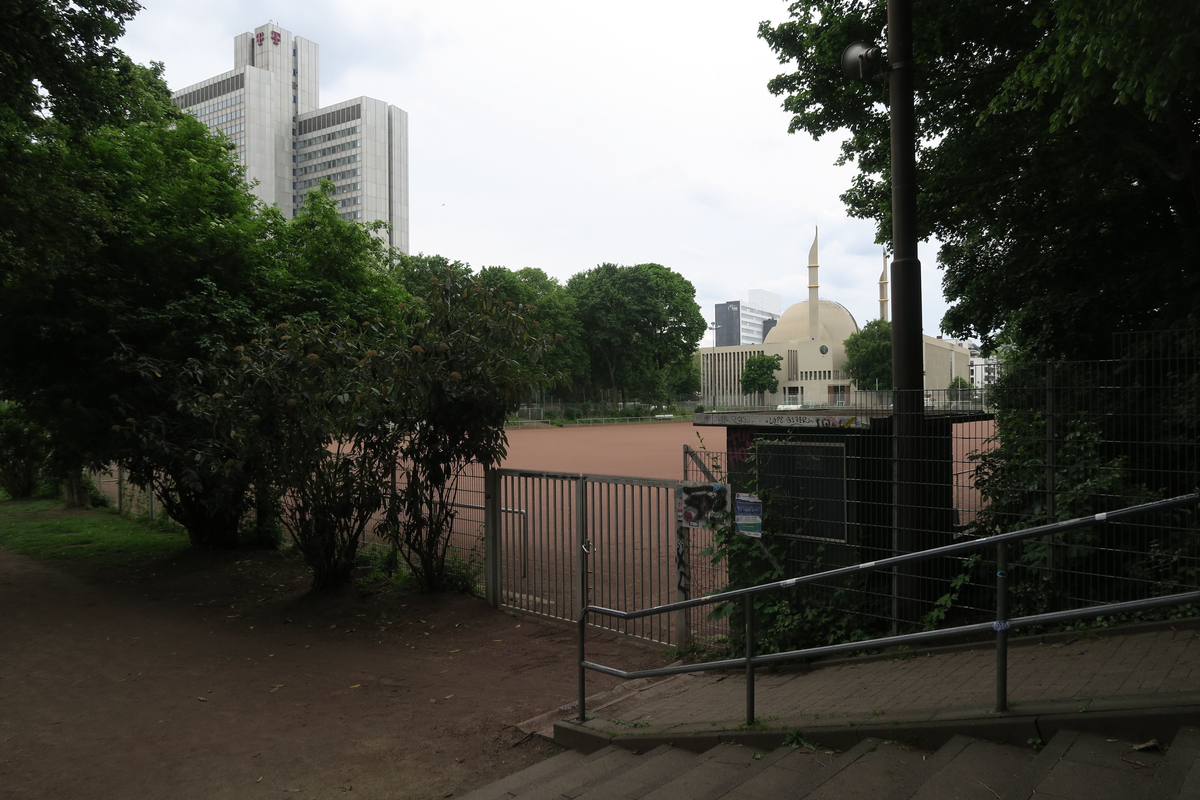 Blick auf einen Fußball-Ascheplatz, dahinter ist die Moschee zu sehen und das Telekom-Hochhaus im Inneren Grüngürtel.