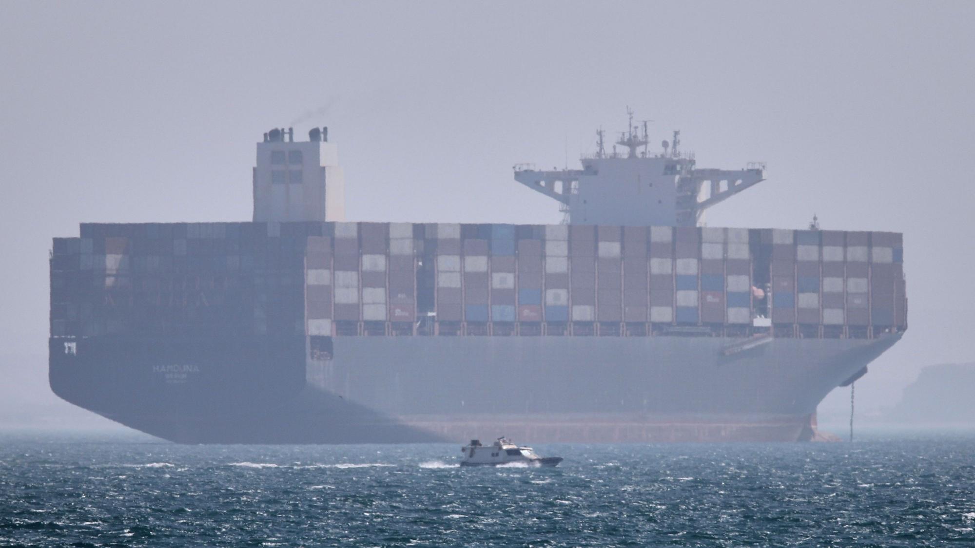 Iran, Bandar Abbas: Ein Containerschiff liegt vor Anker, während im Vordergrund ein kleines Motorboot in der Straße von Hormus vorbeifährt (Archivbild).